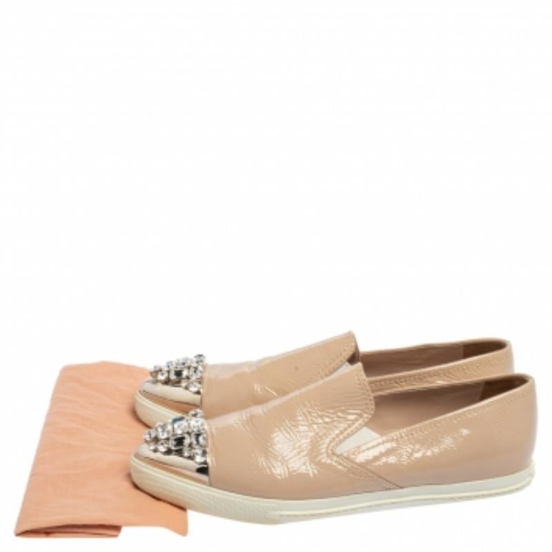Este par de zapatillas slip-on de Miu Miu combina elegancia y estilo. Los zapatos están forrados en charol beige y diseñados con cristales en la puntera. Las zapatillas se asientan sobre suelas de goma para proporcionarte una pisada cómoda.
