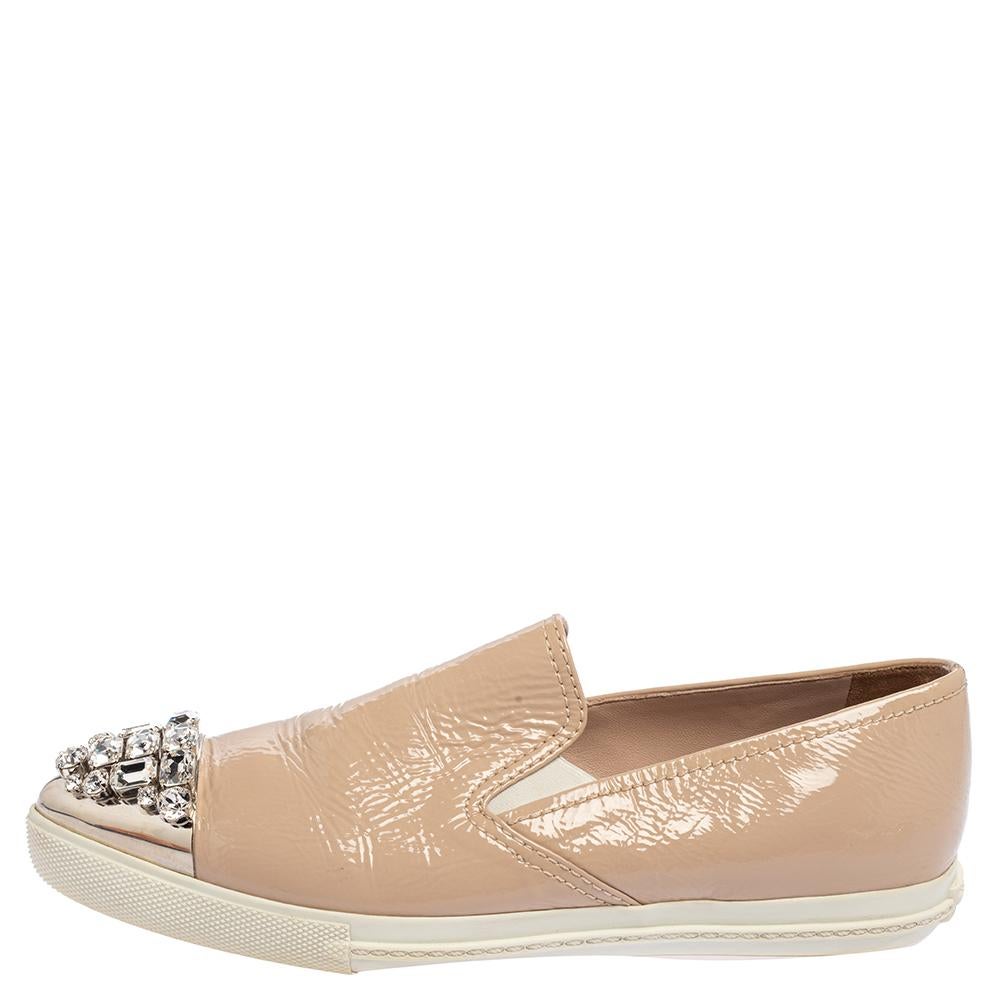 In a fine blend of elegance and style comes this pair of slip-on sneakers from Miu Miu. The shoes are covered in beige patent leather and designed with crystals on the pointed cap toes. The sneakers are set on rubber soles to give you a comfortable