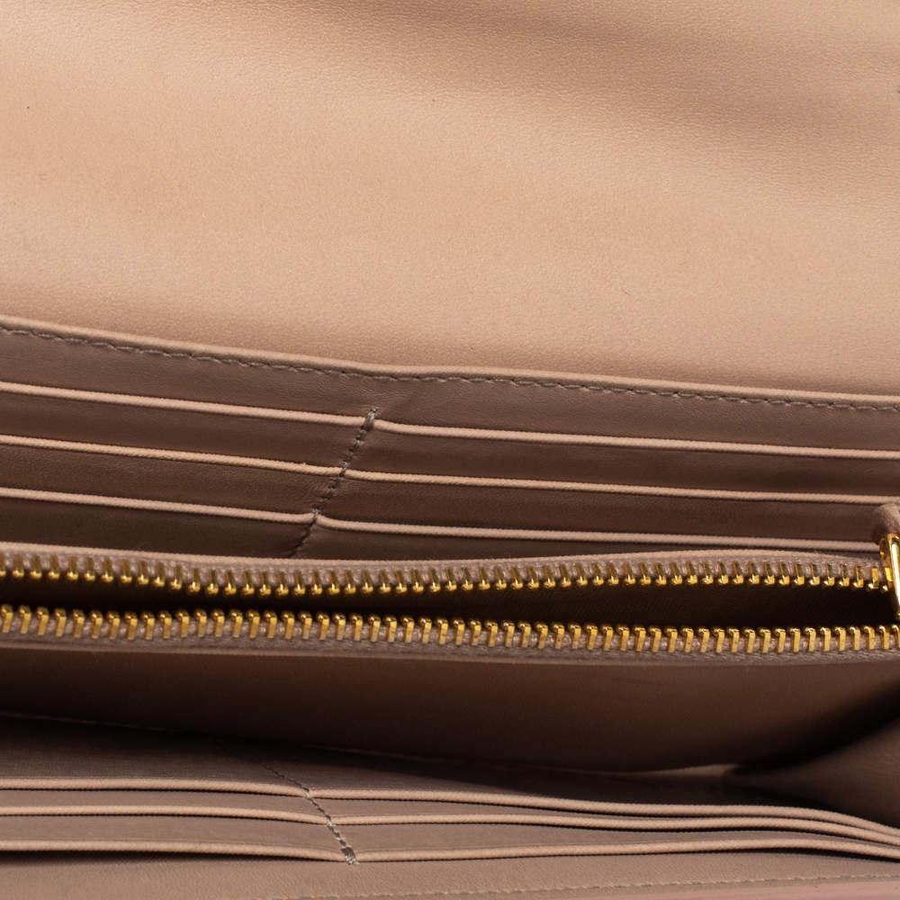 This stylish continental wallet by Miu Miu is stunning. Crafted from quality patent leather, it comes in a versatile shade of beige. It has a front flap with a bow detail that adds interest. It has a leather & fabric interior with enough space for