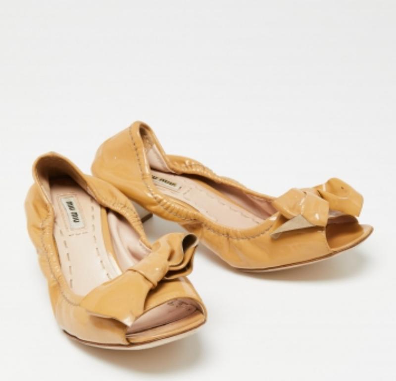 Con estos zapatos de salón de Miu Miu estarás realmente regia, ya que son elegantes y majestuosos. Están confeccionados en charol con puntera abierta, detalles de lazo en la parte delantera e impresionantes tacones con incrustaciones de cristal.