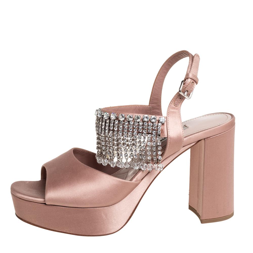 Receive enduring comfort and style with these sandals from Miu Miu. Fashioned in beige satin, the sandals come with open toes, trim of dangling crystals, buckle ankle fastening, block heels, and platforms.

