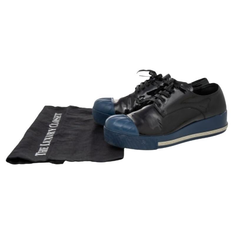 Wer hätte gedacht, dass Turnschuhe so glamourös aussehen können! Diese schwarz-blauen Schuhe von Miu Miu sind aus glänzendem Lackleder und Gummi gefertigt und mit einer CAP-Zehe versehen. Sie weisen Schnürungen an der Leiste auf und sind mit einer