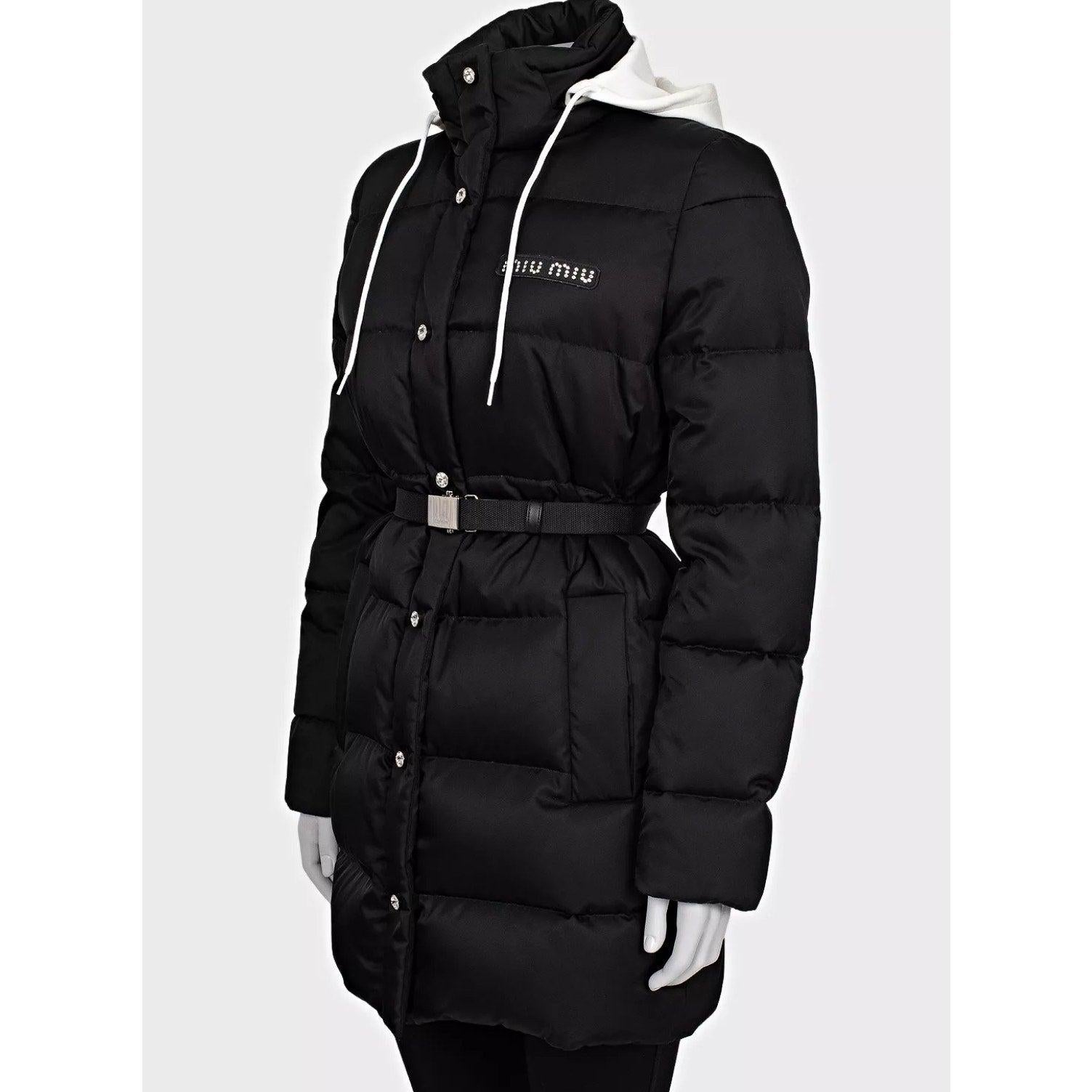 Eleva la tua collezione di capispalla con questa elegante giacca puffer in gabardina nera di Miu Miu. Questo pezzo elegante e funzionale è caratterizzato da dettagli in cristallo e hardware in tonalità argento, che aggiungono un tocco di lusso al