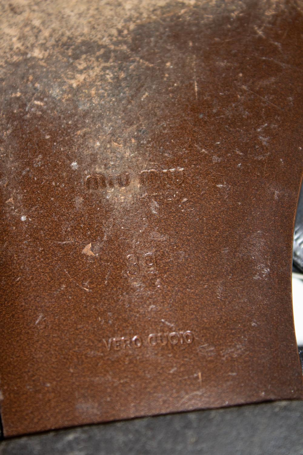Un fantastico paio di sandali estivi di Miu Miu. In pelle nera con dettaglio a catena, le scarpe da ginnastica hanno una suola in cuoio e sono di taglia EU 39.