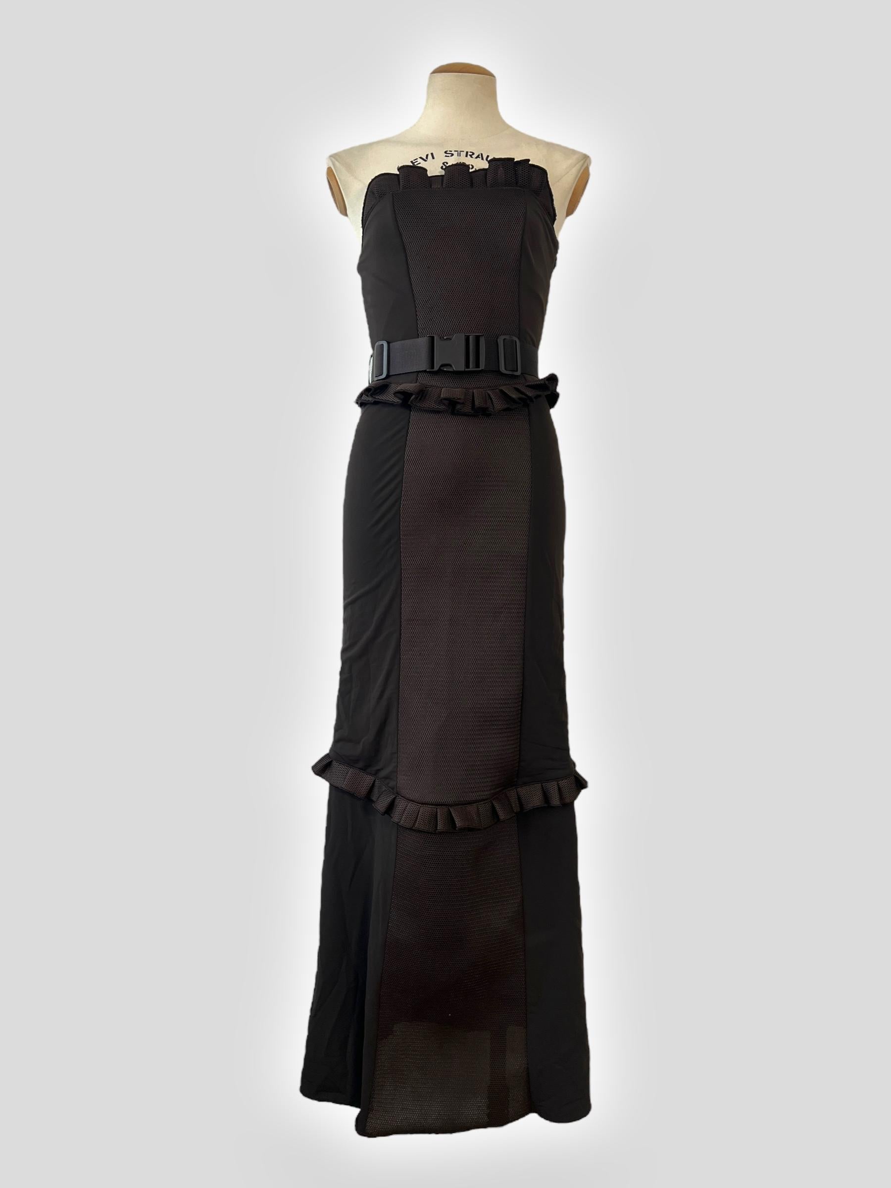 A striking archival piece from Miu Miu’s Fall/Winter 1999 runway collection, this black strapless maxi dress blends utilitarian edge with feminine ruffles. Designed with contrasting textures, the structured bodice features a mix of net fabric and