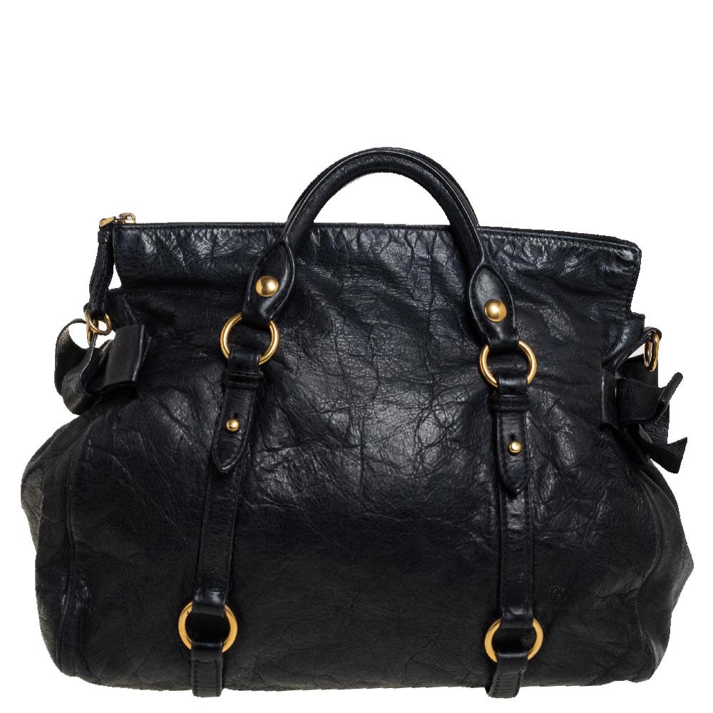 This Bow bag by Miu Miu is an edgy daytime handbag with feminine finishes. This tote bag is made from black Vitello Lux leather with luxe gold-tone hardware. It is accented with a front Miu Miu label, lovely side bows, double flat handles, and a