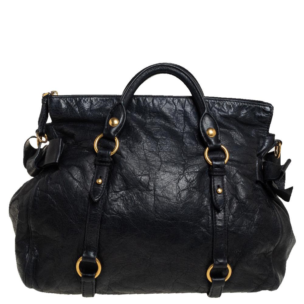 Questa borsa Bow di Miu Miu è una borsetta da giorno dal design elegante e dalle finiture femminili. Questa borsa tote è realizzata in pelle nera di Vitello Lux con finiture dorate di lusso. Presenta un'etichetta Miu Miu frontale, graziosi fiocchi