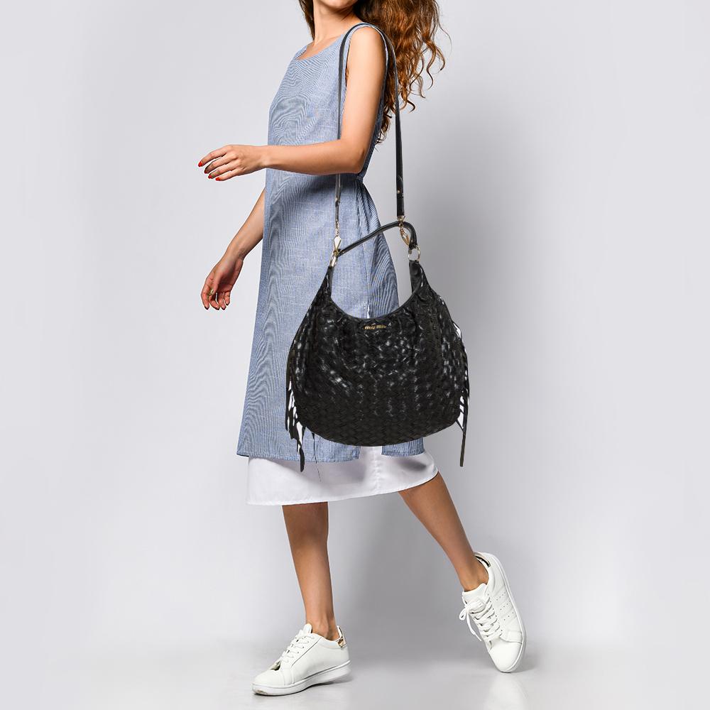 This trendy and spacious Miu Miu Hobo bag is made from intricate woven leather in a beautiful black hue. Equipped with a single handle, a shoulder strap for hands-free carrying option, and gold-tone hardware, it features a top zip closure. Adding to