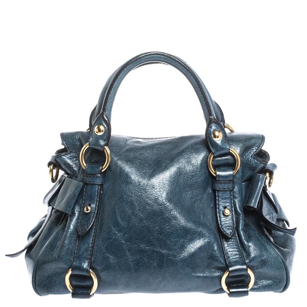 Faites une apparition exquise chaque fois que vous portez ce sac intemporel de Miu Miu. Ajoutez une touche de style à votre look avec cette sacoche bleue. Ce sac en cuir est doté de nœuds sur les côtés:: d'éléments en métal doré et de deux poignées