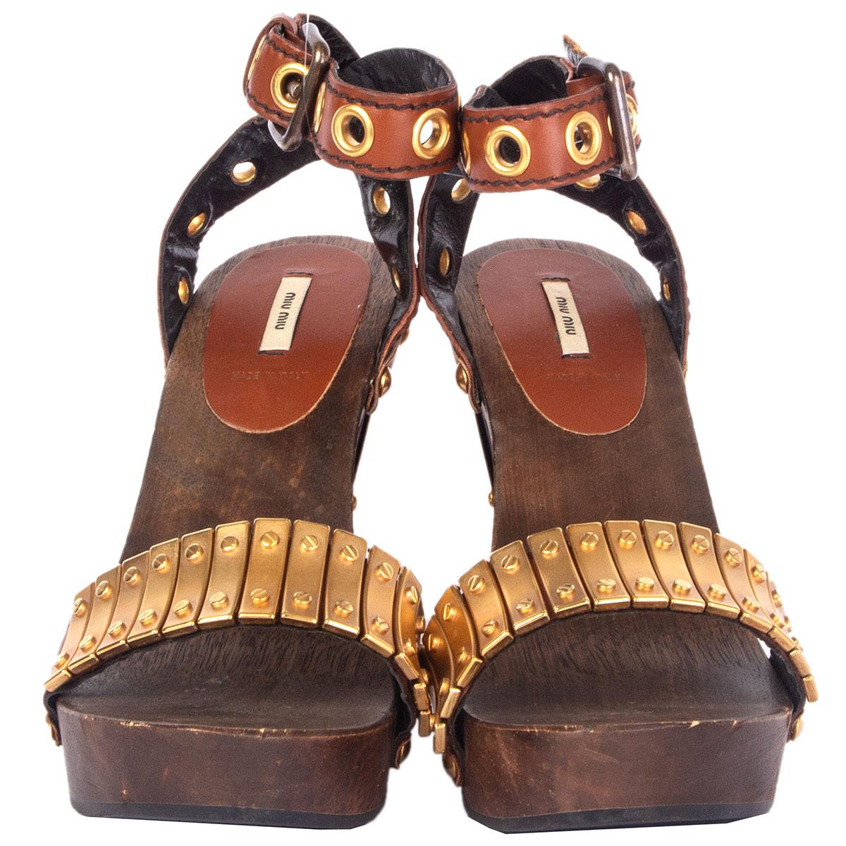100% authentische Miu Miu Sandalen aus braunem Holz und Leder, verziert mit goldfarbenen Metallplatten und Nieten. Haben mit einigen schwachen Dellen auf der hölzernen Plattform getragen worden. Insgesamt in ausgezeichnetem Zustand. Kommt mit