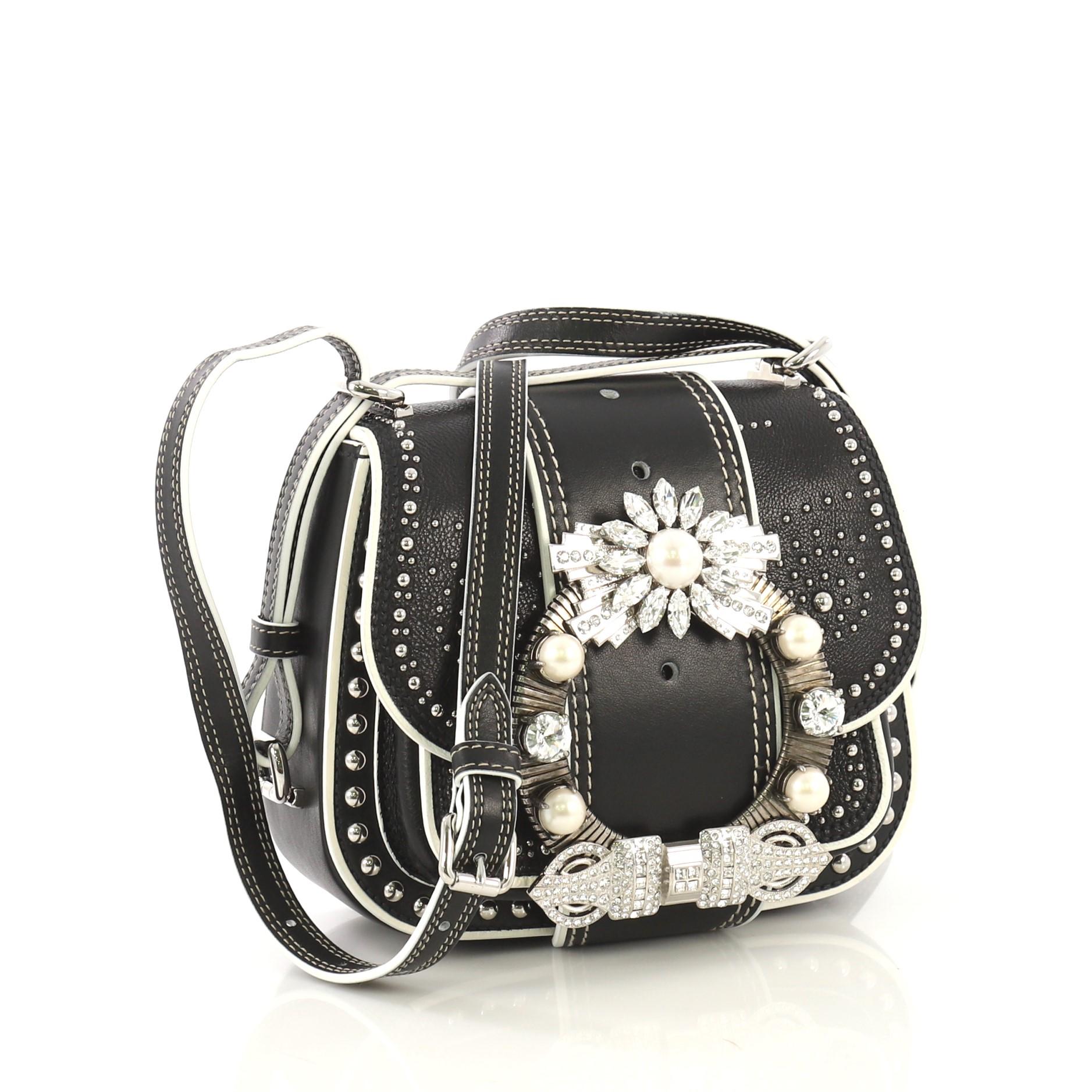 This Miu Miu Dahlia Crossbody Bag Crystal Embellished Leather Small, crafted from black leather, features an adjustable leather shoulder strap, front and back metal studs, front flap with decorative crystal embellishments, and silver-tone hardware.