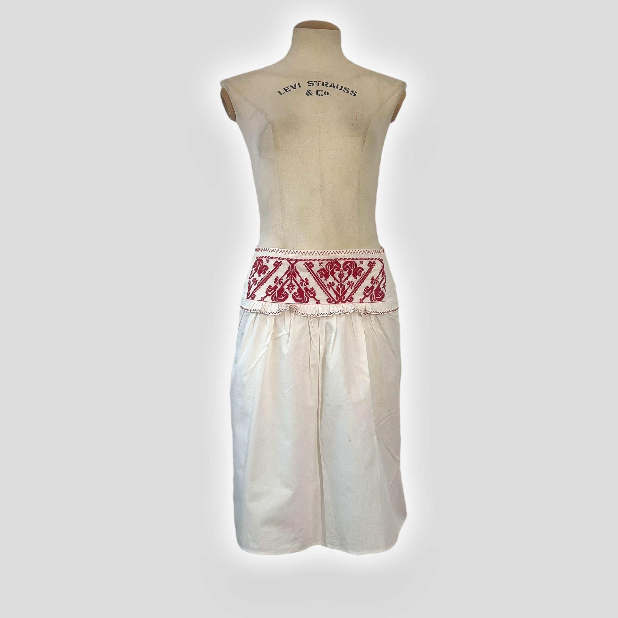 This Miu Miu skirt from 2003 showcases the brand’s signature blend of vintage-inspired craftsmanship and modern femininity. Crafted from crisp white cotton, the design features a striking red embroidered waistband with intricate detailing,