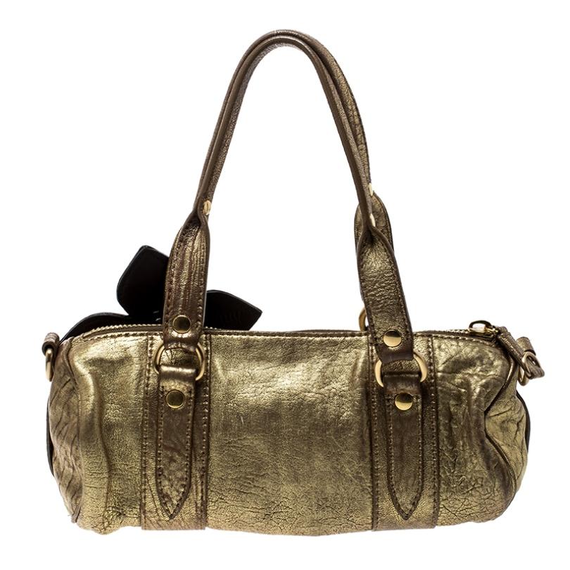 Visually appealing and incredibly stylish is this gold shoulder bag crafted from high-quality leather. Look graceful and urbane in this Miu Miu creation that has two handles, a fabric interior, and a flower applique on the front.

Includes: The