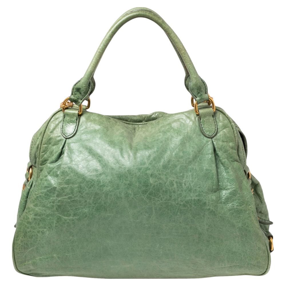 Die Charm Satchel aus dem Hause Miu Miu ist hier, um Ihren Auftritt aufzuwerten und Sie umwerfend aussehen zu lassen. Sie ist aus grünem Leder gefertigt und hat einen goldfarbenen Charme, der an der Vorderseite herunterhängt. Sie hat zwei Griffe,