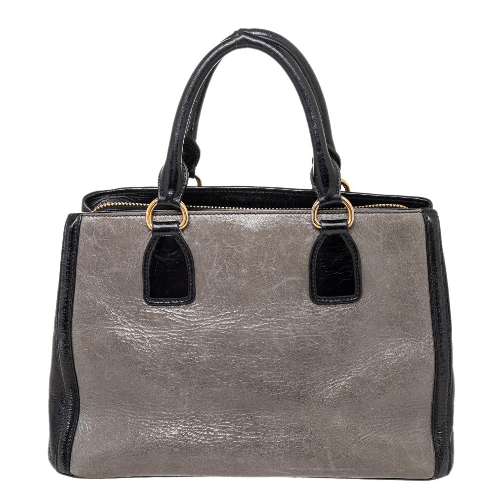This elegant Madras tote from Miu Miu will make a valuable addition to your collection. The tote is crafted from grey and black leather and features a spacious silhouette. It has dual handles and a fabric-lined interior that can hold all your daily