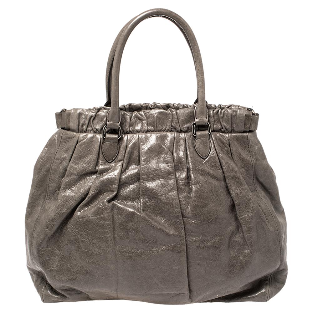 Miu Miu brings you this lovely gathered tote that has been crafted from grey glazed leather. It has a well-sized satin interior and the bag is complete with two top handles and a shoulder strap. Stylish and ideal for daily use, this bag is a worthy