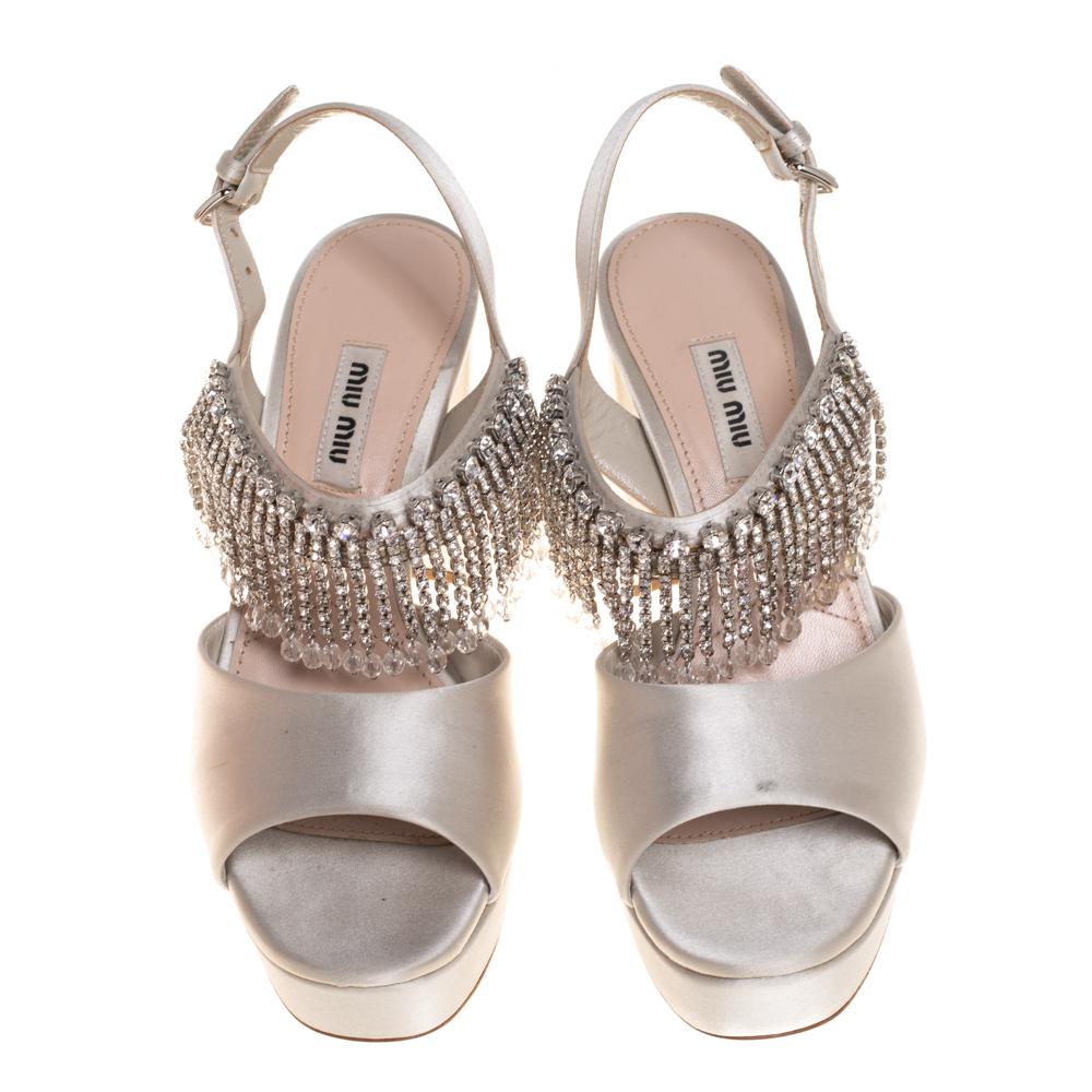 Exuding a glamorous style and polished finish, these Miu Miu sandals are crafted from grey satin. They rest on block heels supported by chunky platforms. They are made opulent with dangling crystal embellishments on the vamps that will flutter