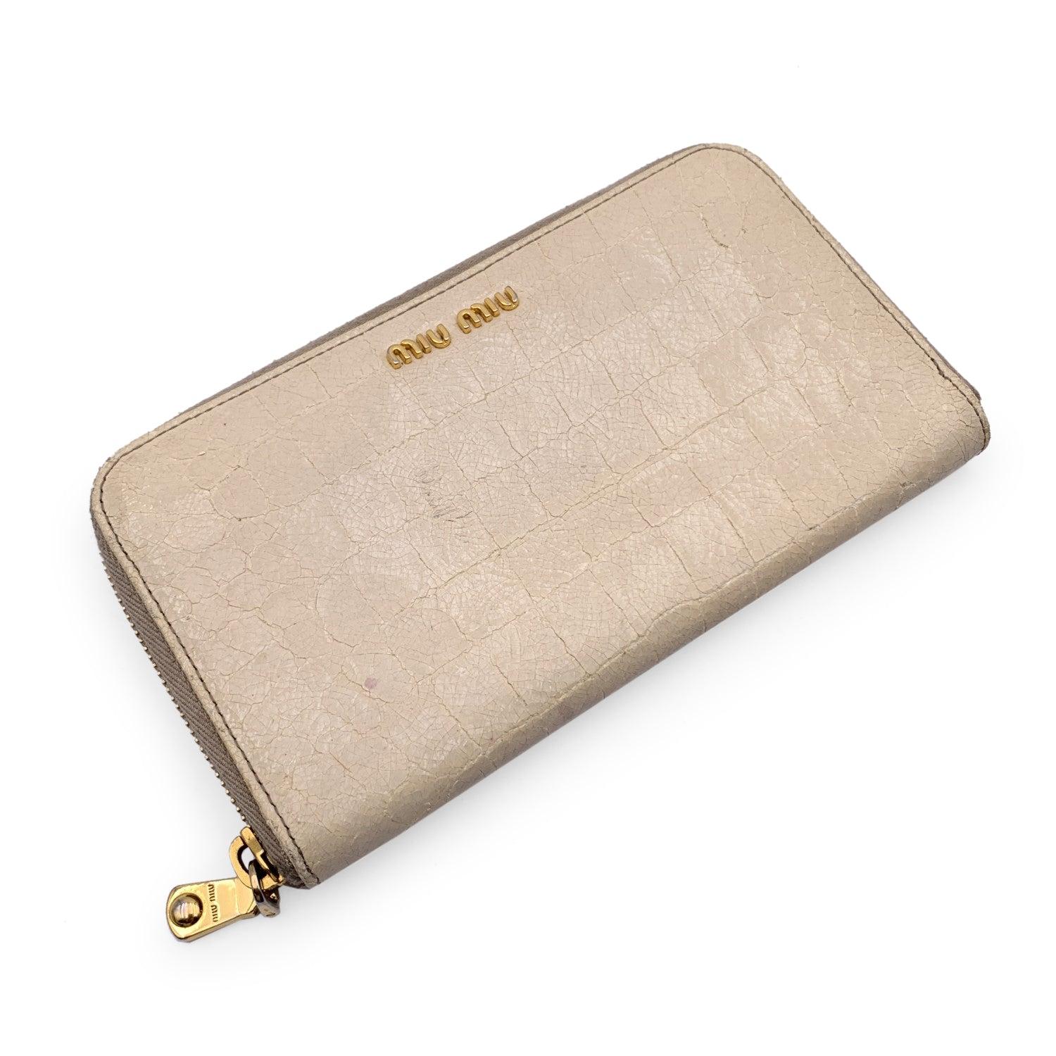 Miu Miu Zippy Wallet crafted in light beige embossed leather. Zip closure. It features 2 main compartments for bill, 2 flat open pockets, 1 zip coin compartment, 8 credit card slots. Gold metal MIU MIU lettering on the front. 'Miu Miu' and 'Made in