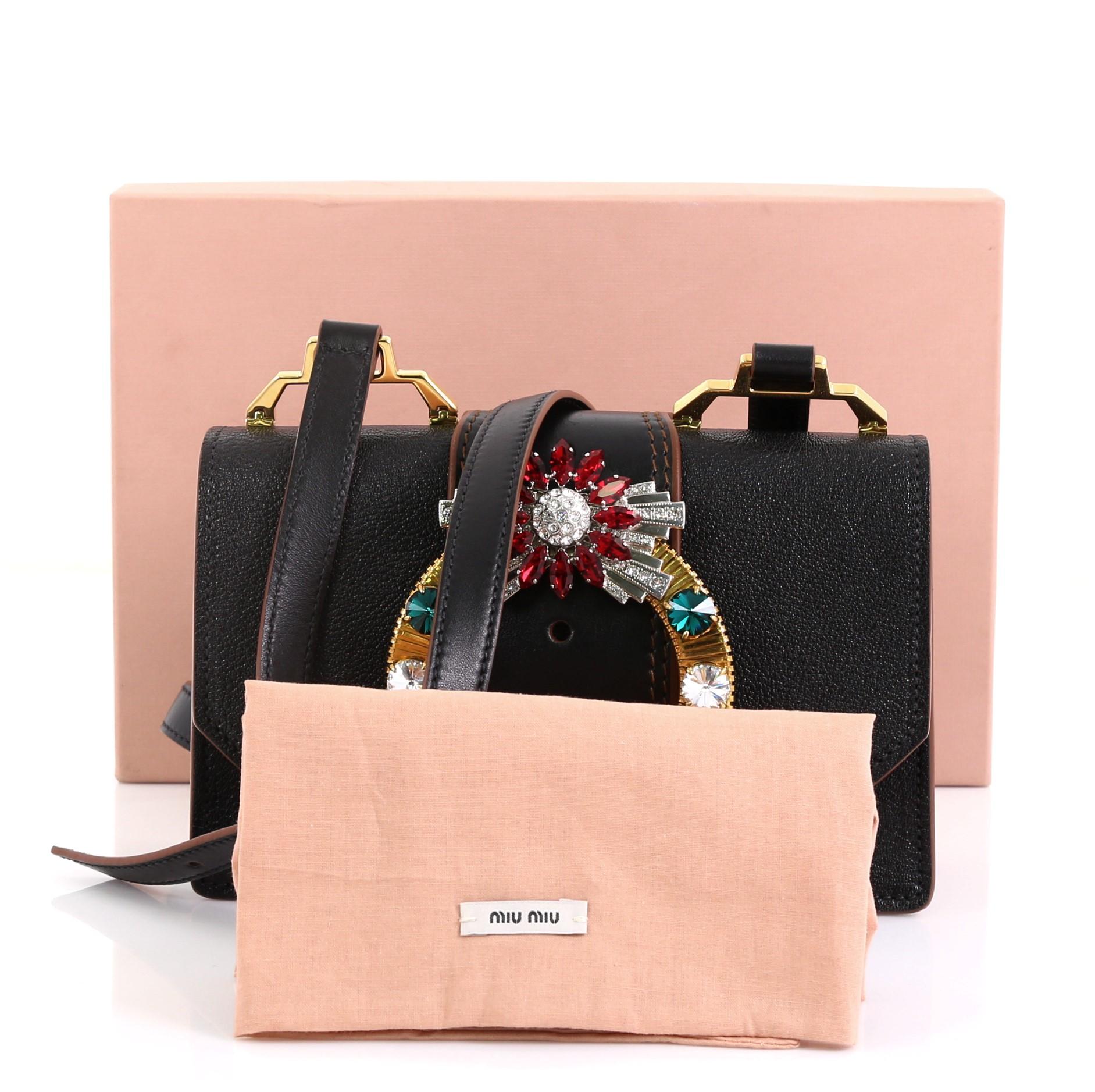 This Miu Miu Madras Crystal Buckle Shoulder Bag Leather Small, crafted in black leather, features an adjustable leather shoulder strap, crystal-embellished giant buckle, and gold-tone hardware. Its magnetic snap button closure opens to a black suede
