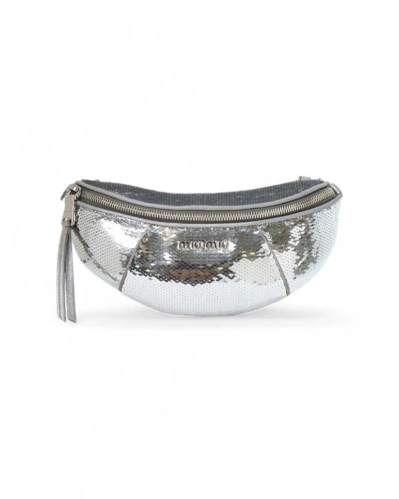 Marsupio firmato Miu Miu, misura small, realizzato in pelle argento arricchita da paillettes e hardware tono su tono. Dotato di una chiusura semicircolare a zip, internamente rivestito in tessuto nero, capiente per l’essenziale. Munito di una