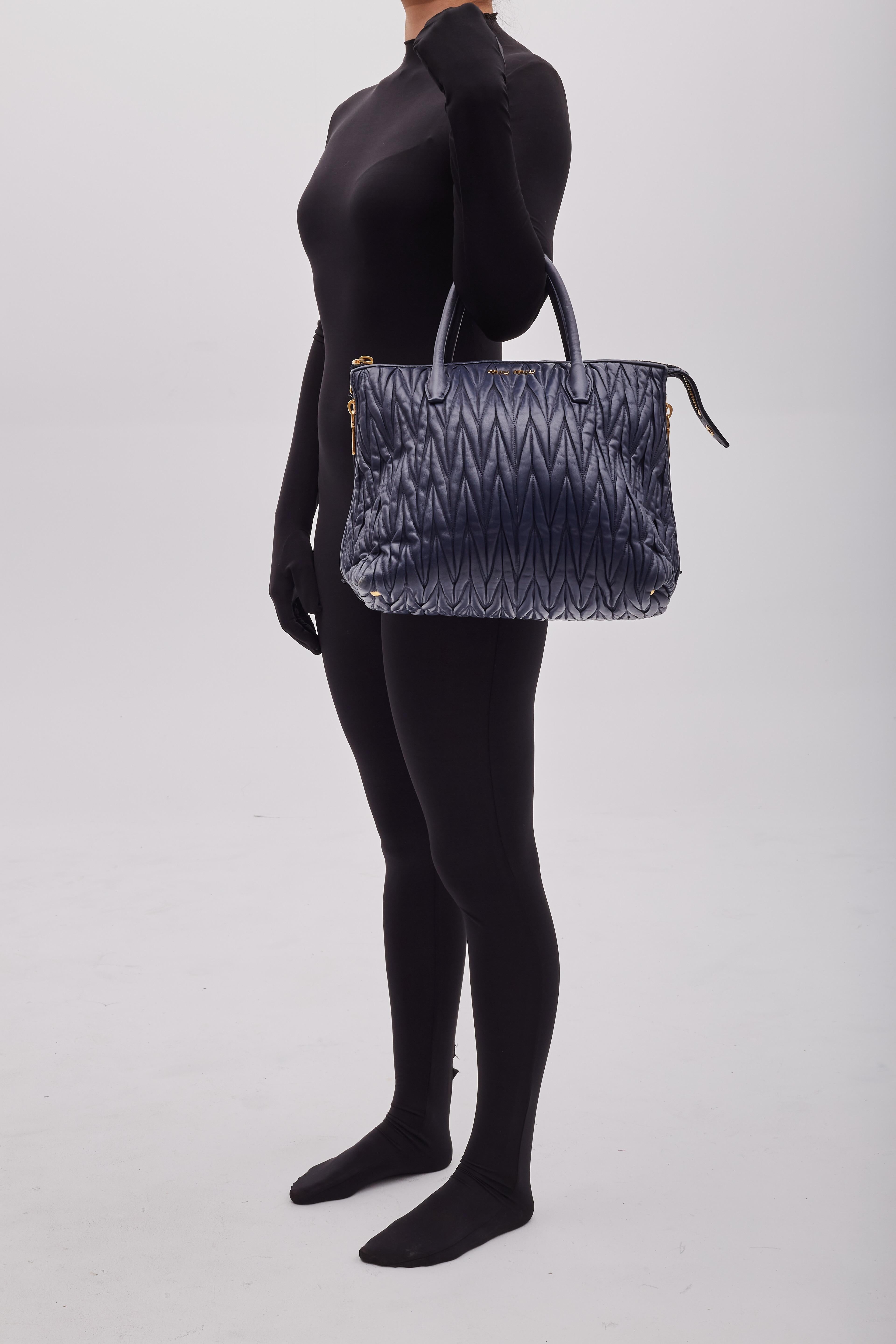 Die MIU MIU Tote Bag, entworfen von Miuccia Prada unter der Marke Miu Miu, wird vorgestellt. Die Tasche hat ein Matelasse-Design, ist aus navyfarbenem Nappaleder gefertigt und mit einer Chevron-Naht akzentuiert. Das unifarbene Muster und die
