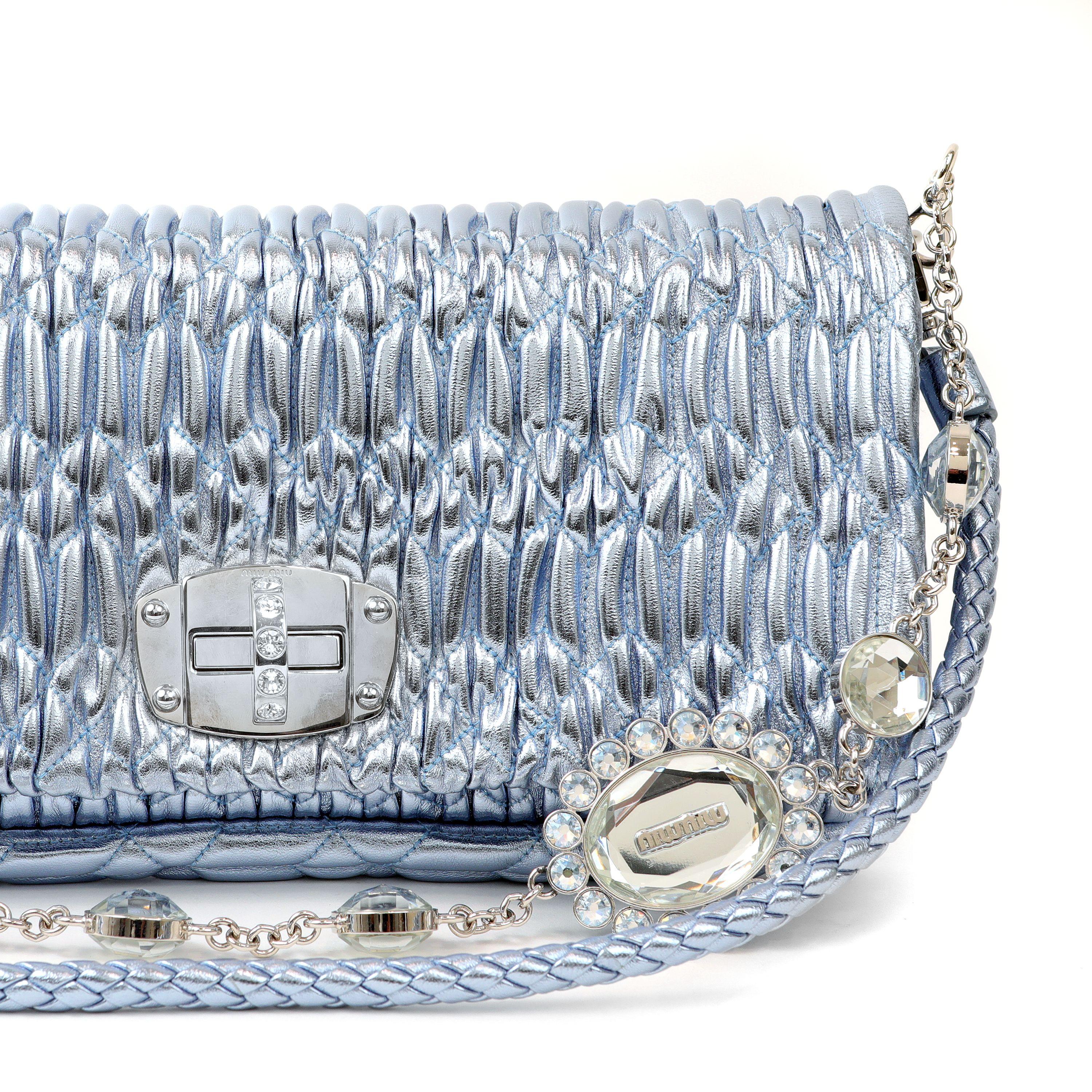 This authentic Miu Miu Metallic Blue Crystal Cloquè Small Bag is in pristine condition.  The iconic design features frosty blue raised quilted Nappa leather with silver and crystal turn lock closure.  May be carried by the detachable leather strap
