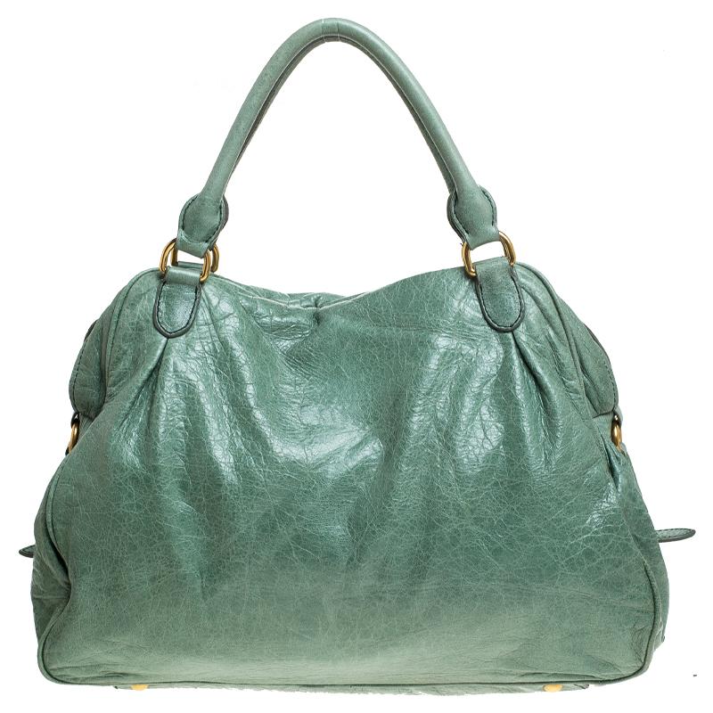 Stunning in appeal and simple in design, this satchel by Miu Miu will be a valuable addition to your closet. Crafted from green distressed leather, it features a front pocket with a lock charm zipper and buckle detailing on the sides. The bag comes