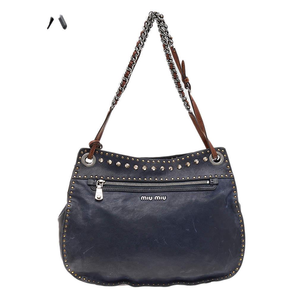 This lovely shoulder bag is from Miu Miu. Meticulously crafted using leather, it comes in a shade of navy blue and brown. It has chain-detailed handles, studs on the exterior, and a suede-lined interior.

Includes: Info Booklet