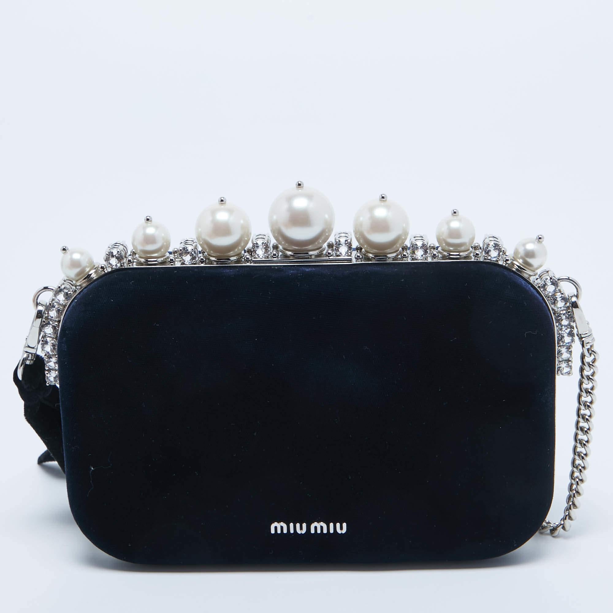 The Miu Miu cutch exudes opulence with its plush navy velvet exterior adorned with exquisite pearls and crystals. The boxy silhouette is complemented by a delicate chain, creating a luxurious and sophisticated accessory for formal