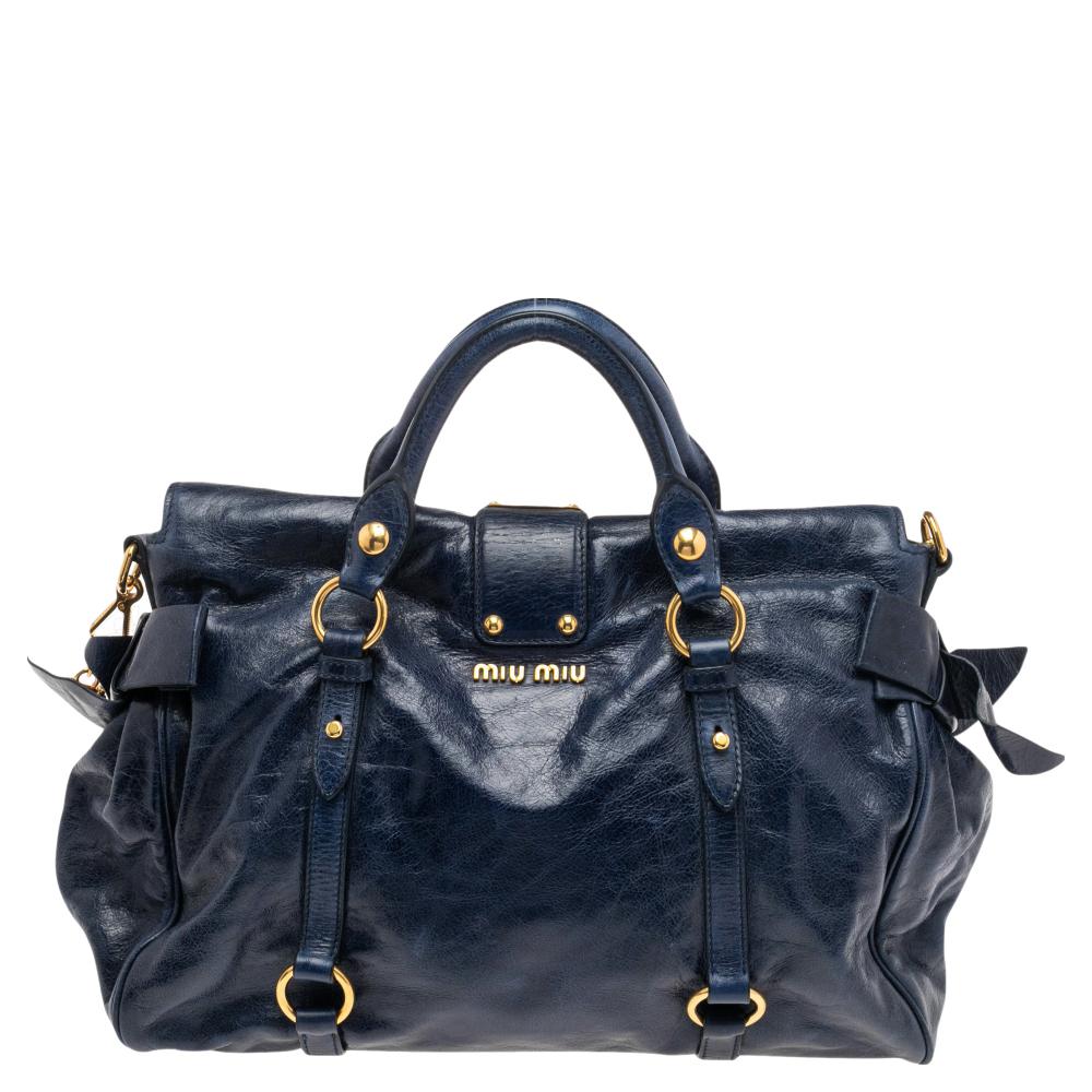 Masterfully crafted from Vitello Lux leather and lined with satin, this satchel from the house of Miu Miu is both stylish and durable. In a shade of navy blue, it flaunts dual top handles and noticeable bows on the sides. Equipped with a detachable