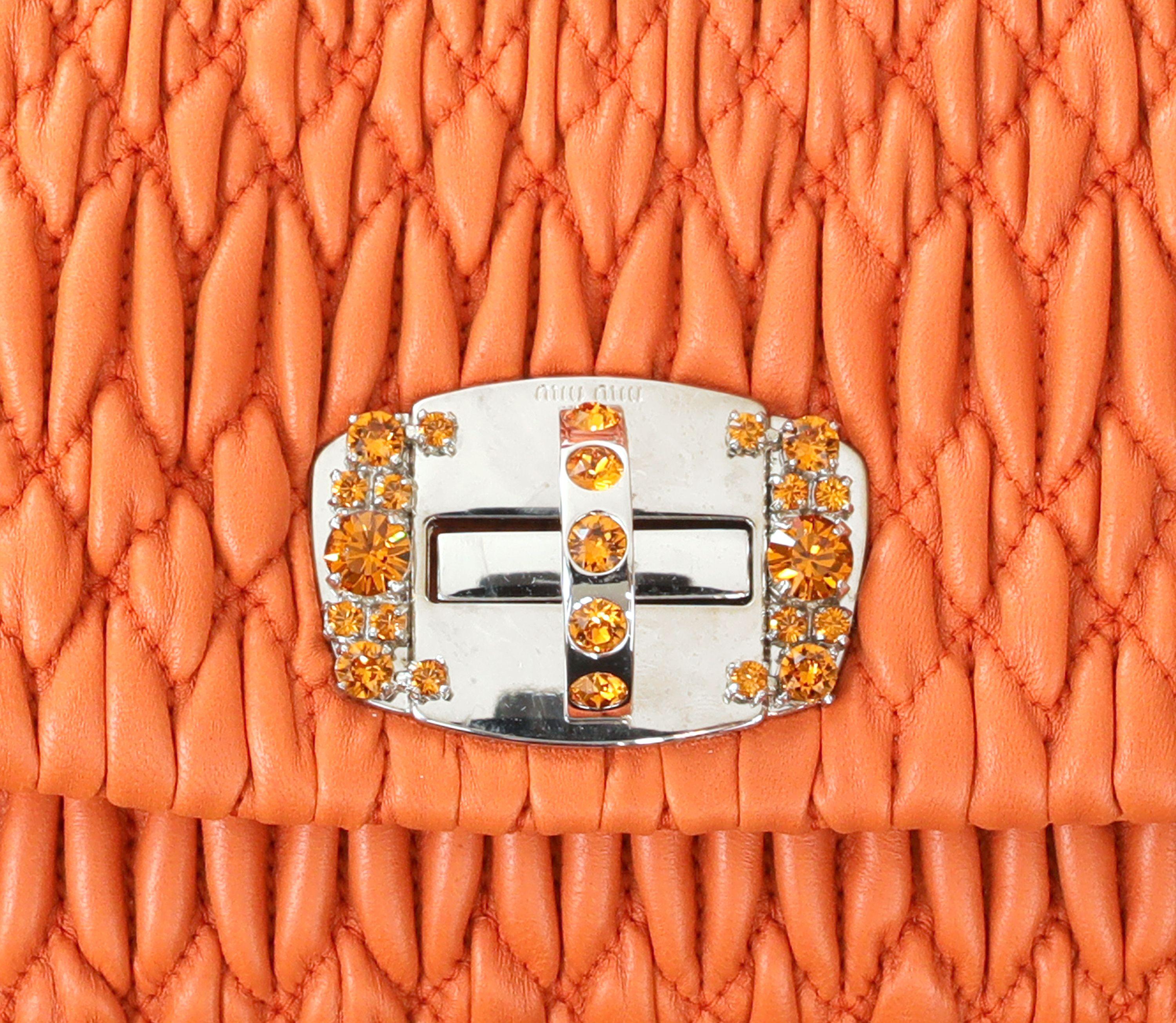 Cet authentique petit sac Miu Miu Orange Crystal Condit est en parfait état.  Ce modèle emblématique est doté d'un cuir Nappa matelassé orange et d'une fermeture à verrou tournant en cristal.  Peut être porté avec la lanière de cuir amovible ou la