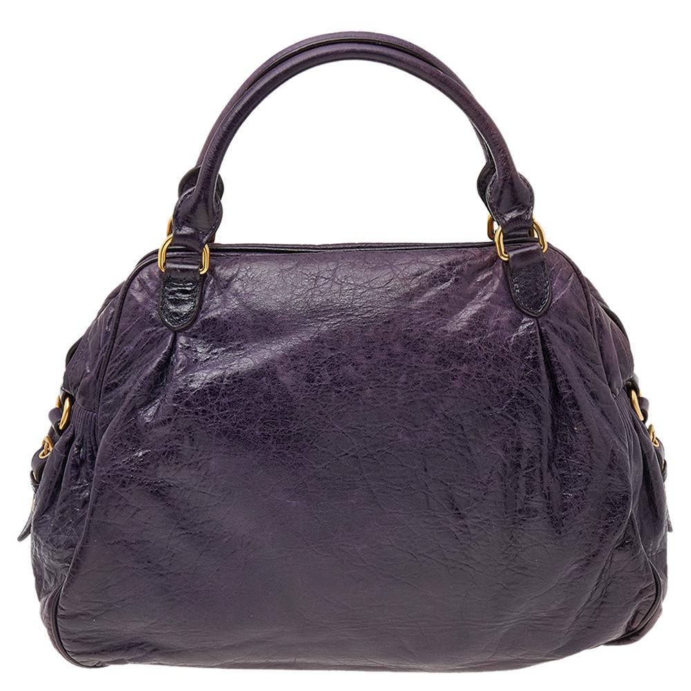 Stunning in appeal and simple in design, this satchel by Miu Miu will be a valuable addition to your closet. Crafted from purple distressed leather it features a front pocket with a lock charm zipper and buckle detailing on the sides. The bag comes