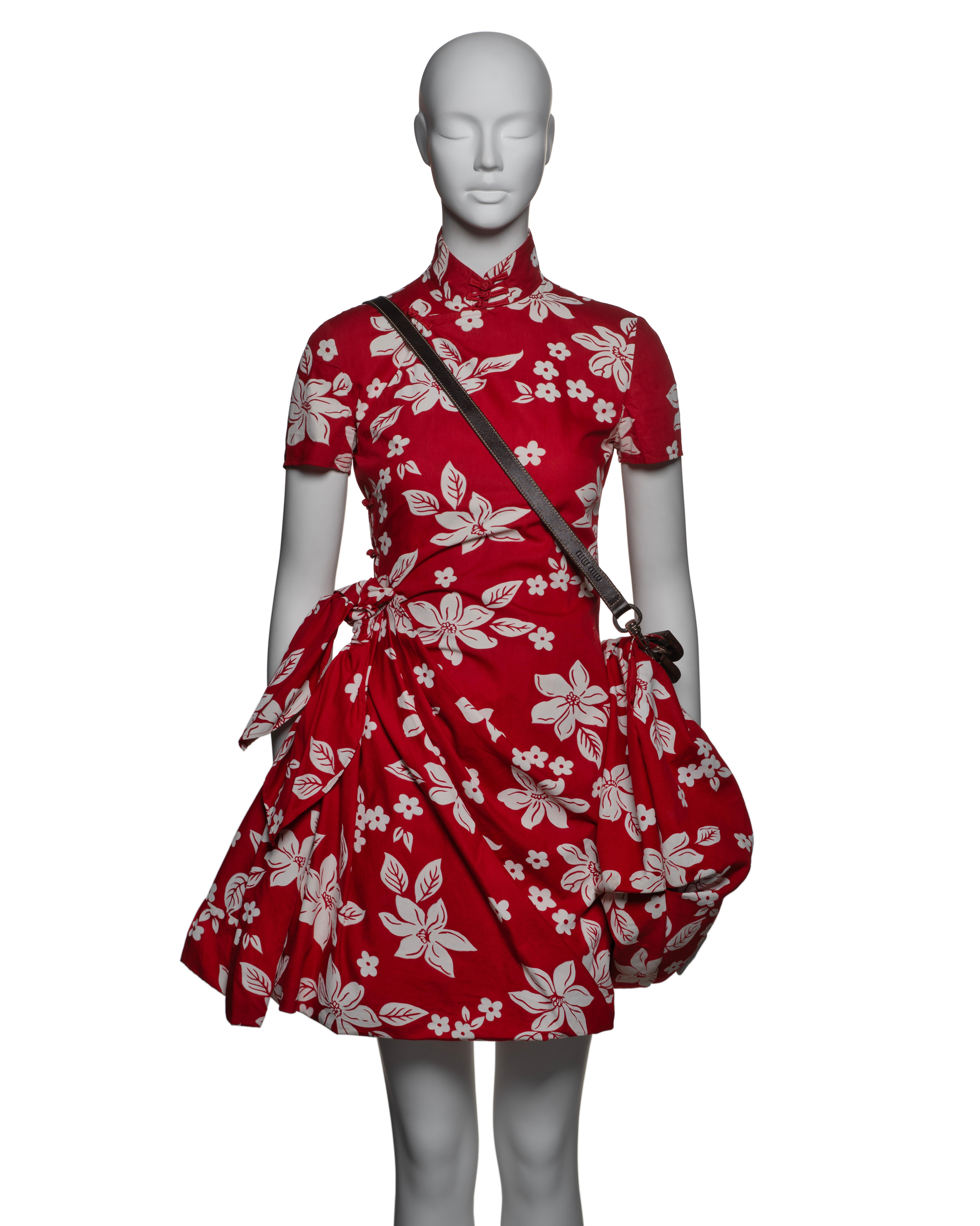 This Miu Miu ensemble features a cheongsam-inspired red cotton mini dress adorned with an all-over white Hawaiian floral print. The dress showcases a traditional mandarin collar with a short sleeve design and a flattering wrap-style front skirt that