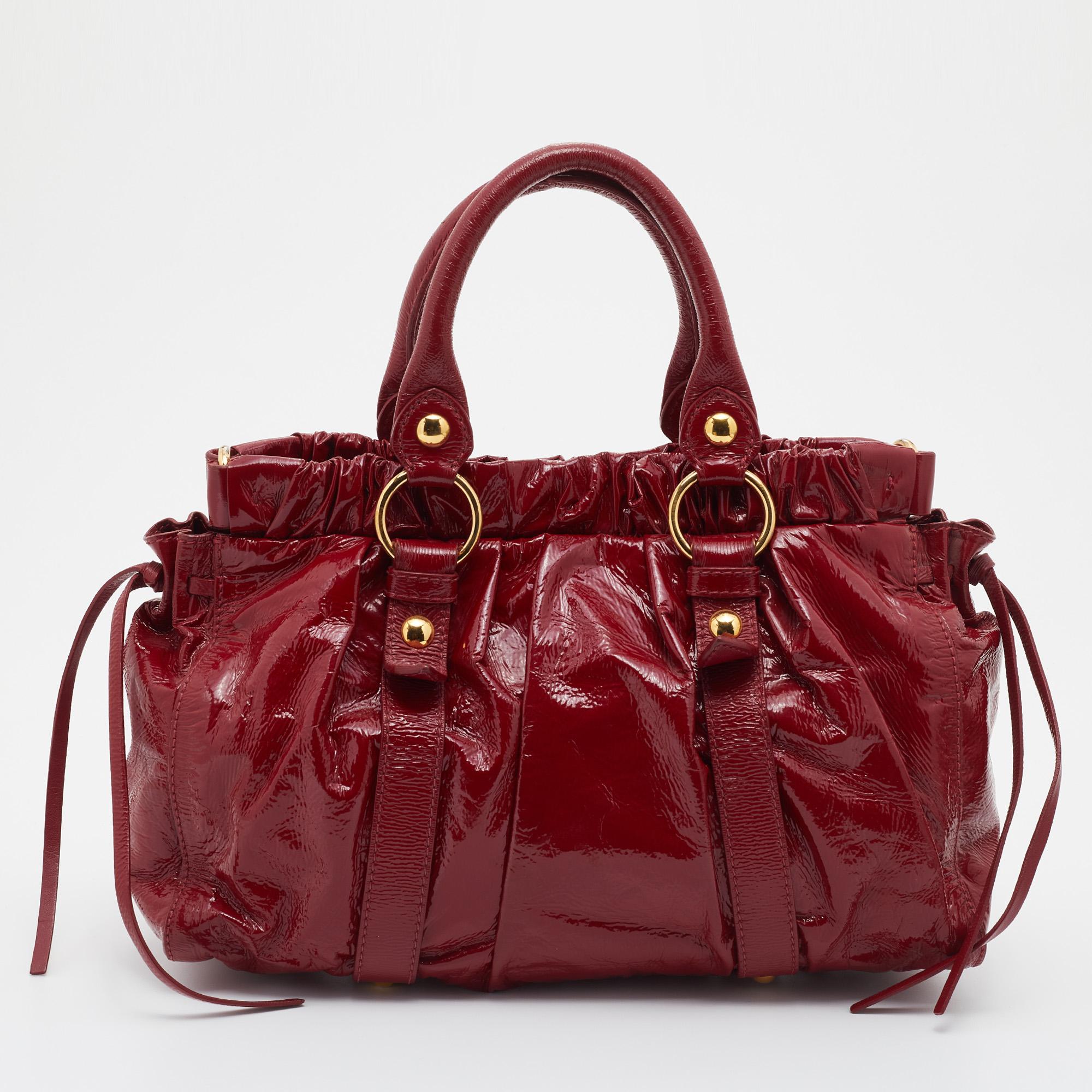 Ce fourre-tout Miu Miu, qui témoigne de la créativité et de la vision de la marque, est réalisé en vernis et de couleur rouge. Il est conçu dans un intéressant style froncé et possède deux poignées supérieures ainsi qu'une bandoulière amovible. Le