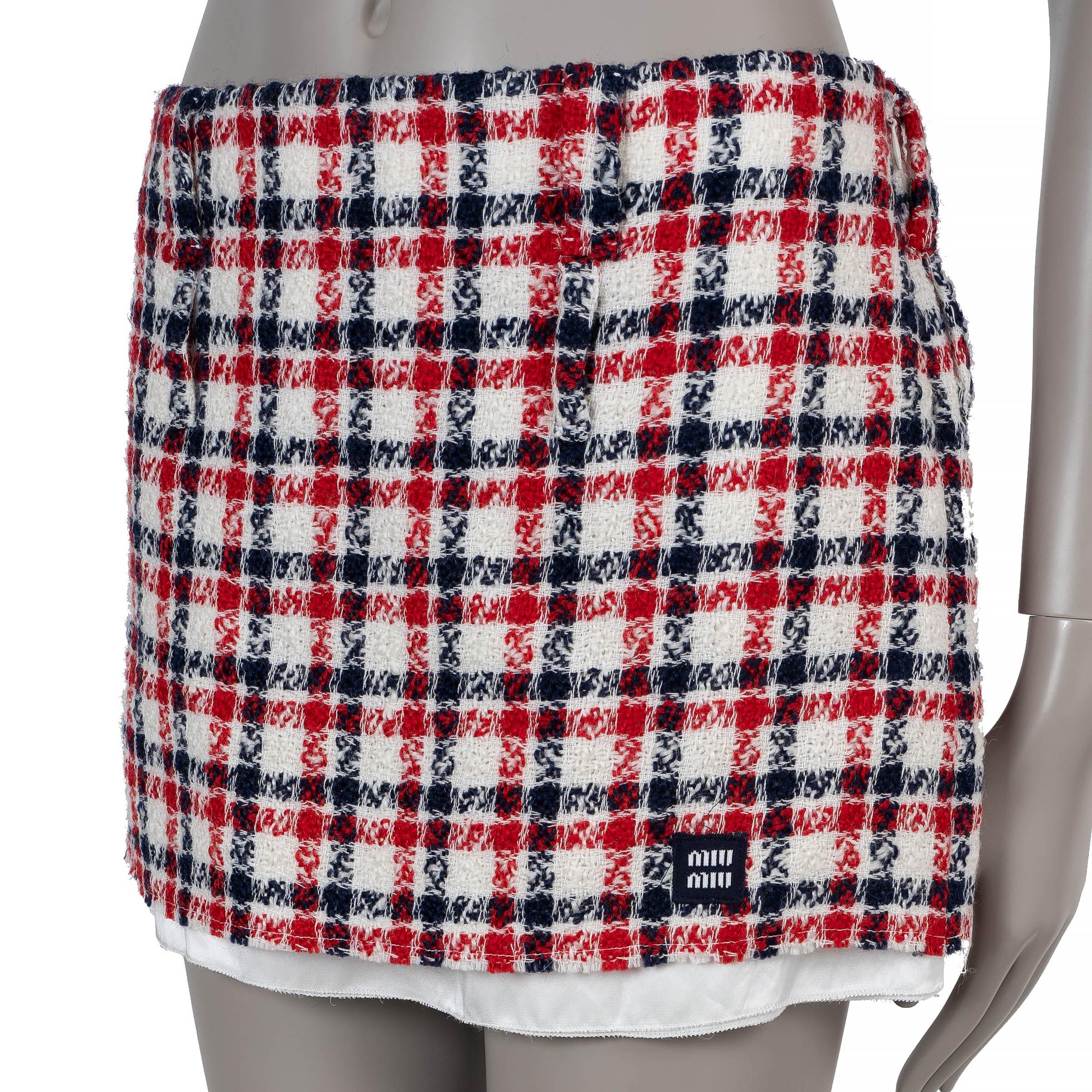 This 100% authentic Miu Miu mini skirt in red, white, and blue plaid tweed wool (100%) offers a playful yet refined take on classic tailoring. Designed with a straight cut, it features an exposed raw-finished white acetate-cupro lining for a