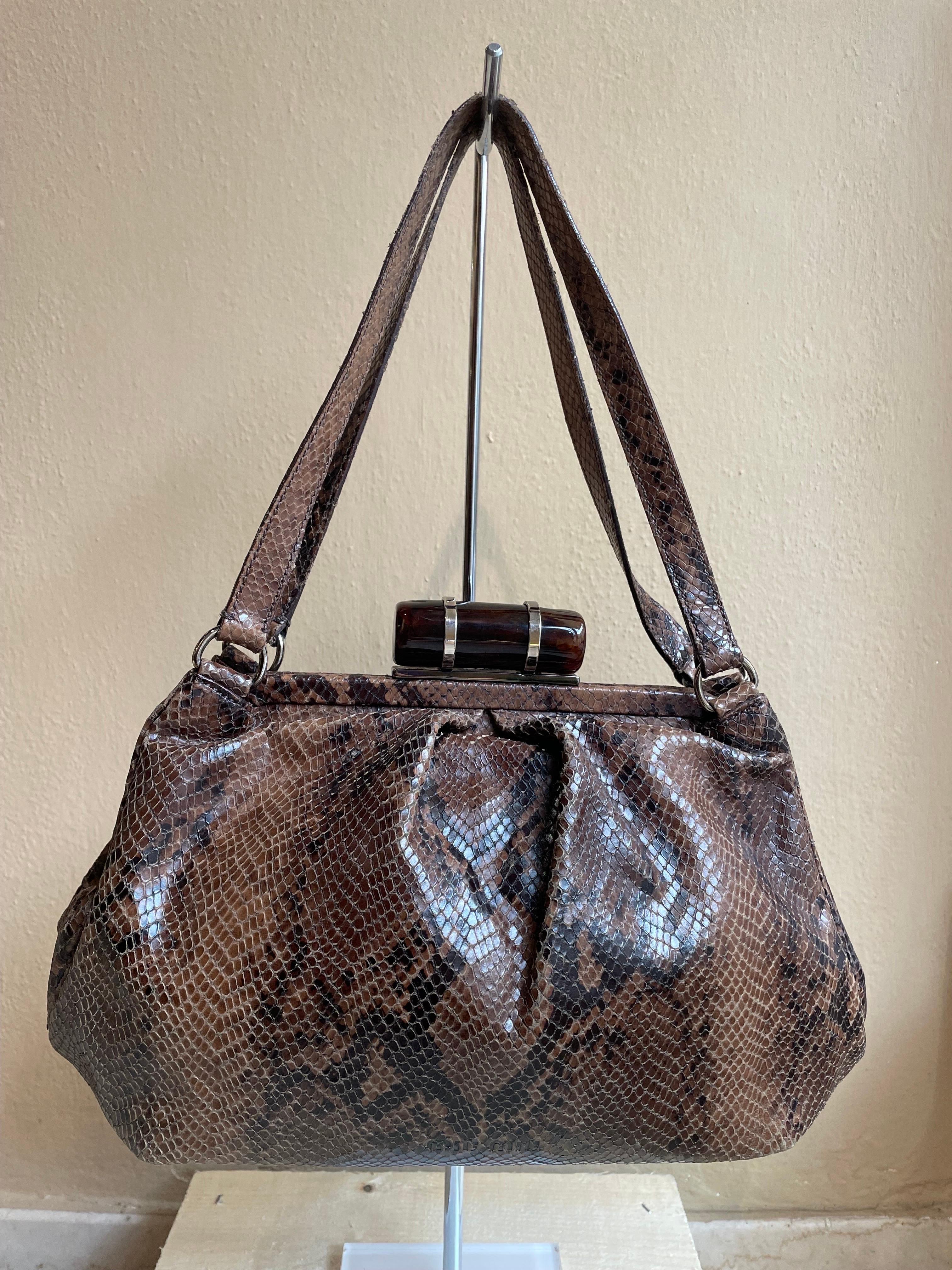Miu Miu reptile bag in shades of brown. Interlocking wood-effect resin closure. Silver hardware. It has some signs of use as you can see from the photos but nothing serious to report. Interior consists of a large pocket plus a side pocket closed