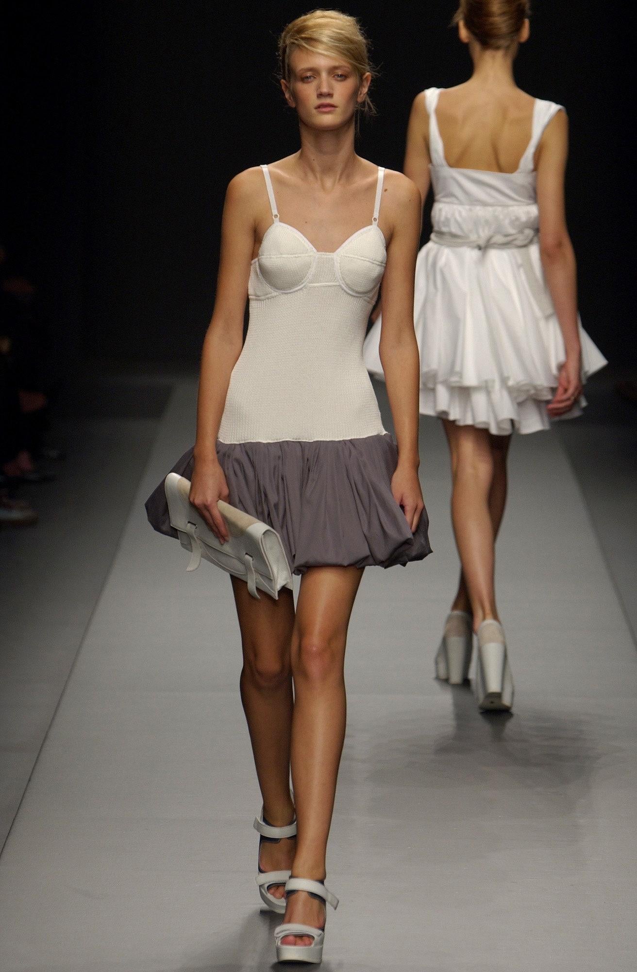 - Designed by Miuccia Prada
- Sold by Skof.Archive
- Spring Summer 2003 Collection
- Runway Piece
- White ribbed knit dress with contrasting grey pleated skirt
- Bustier-style cups with grey trim detailing
- Thin white shoulder straps
- Form-fitting