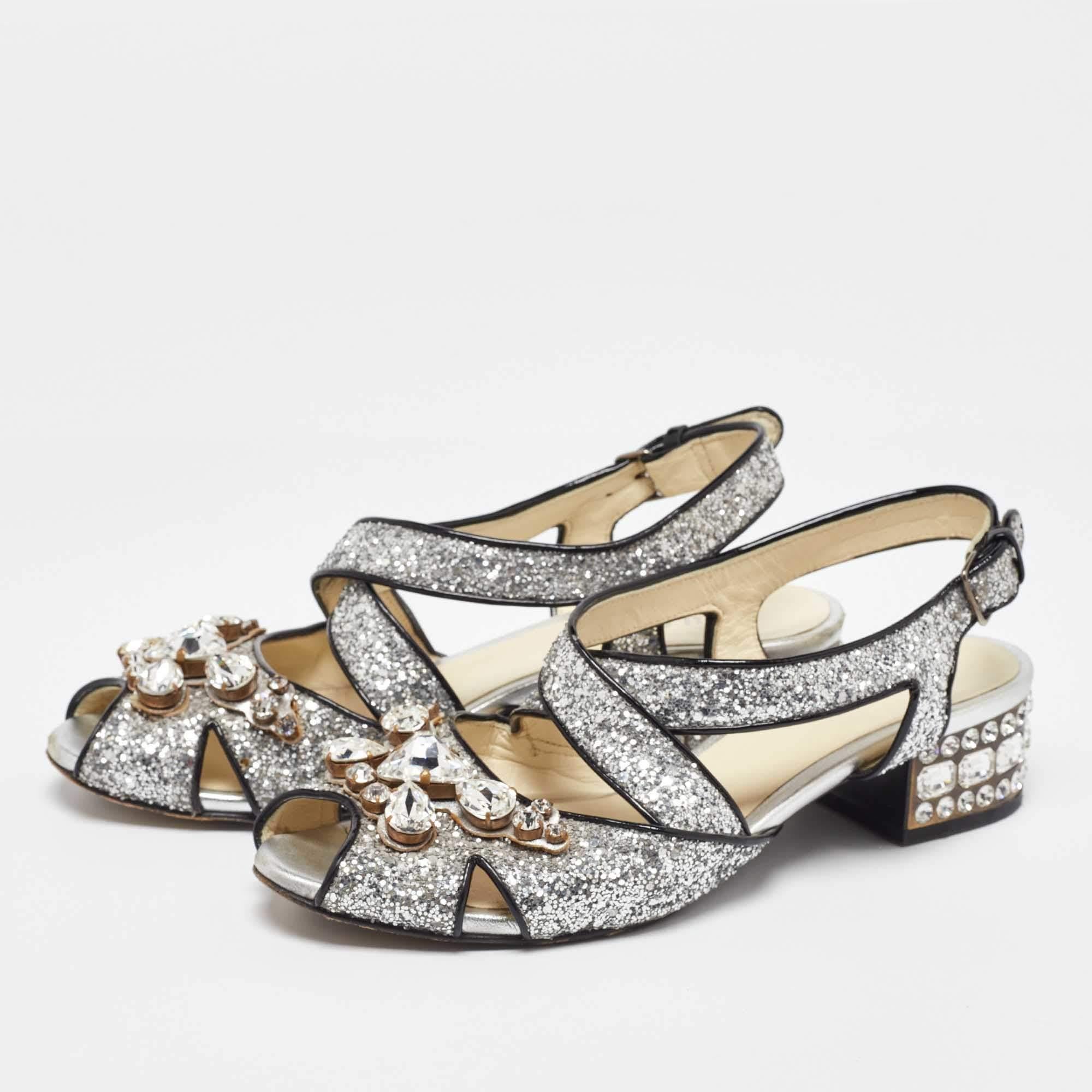 Zeigen Sie Vielseitigkeit mit diesen Sandalen aus dem Hause Miu Miu. Sie sind aus silbernem Glitter gefertigt und mit Kristallverzierungen auf der Vorderseite versehen. Sie zeigen Blockabsätze mit silberfarbener Hardware und einen