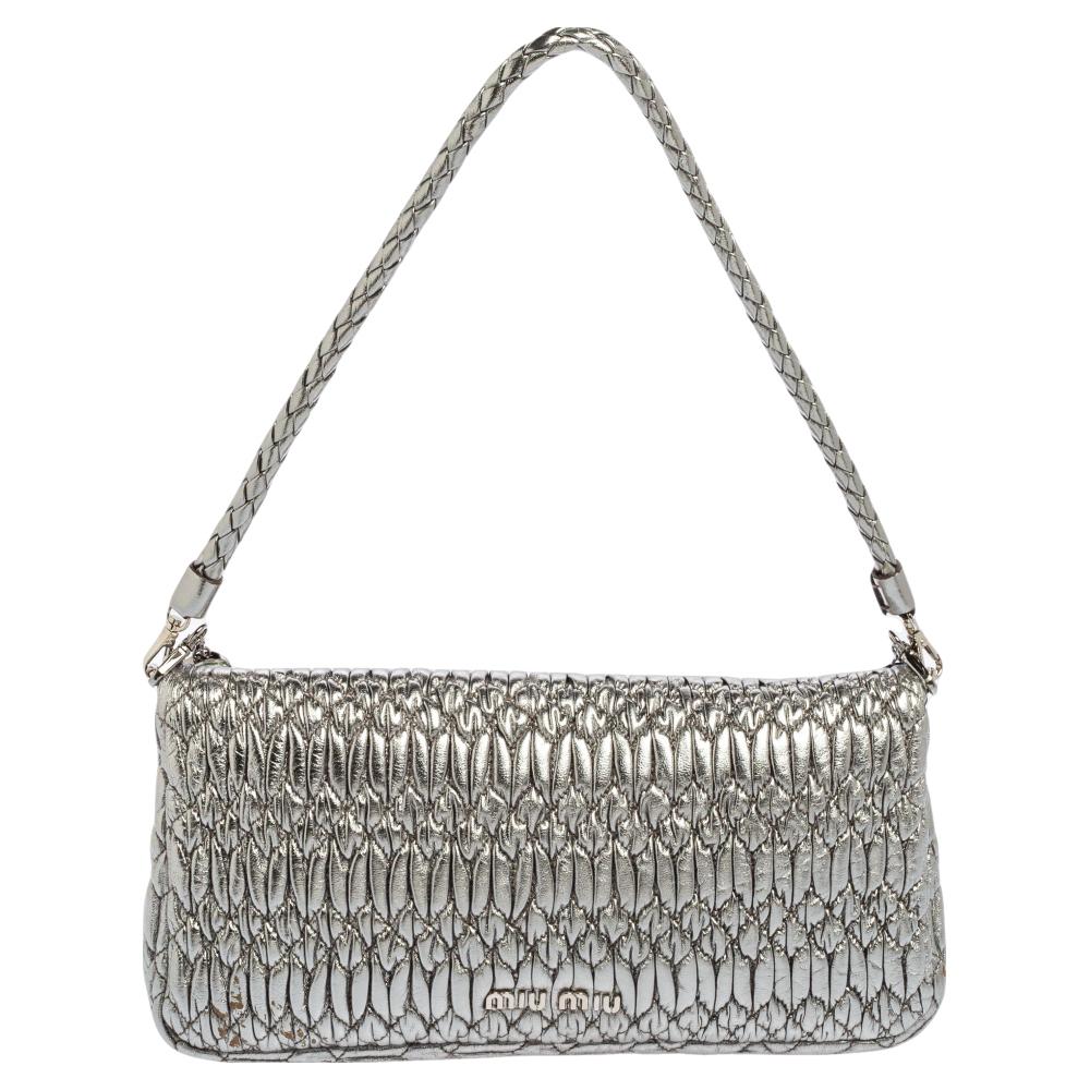 This shoulder bag from the House of Miu Miu displays an eternal design that is a splendid mixture of style and utility. It is made from silver matelassé leather on the exterior with a crystal-embellished lock adorning the front. It reveals a