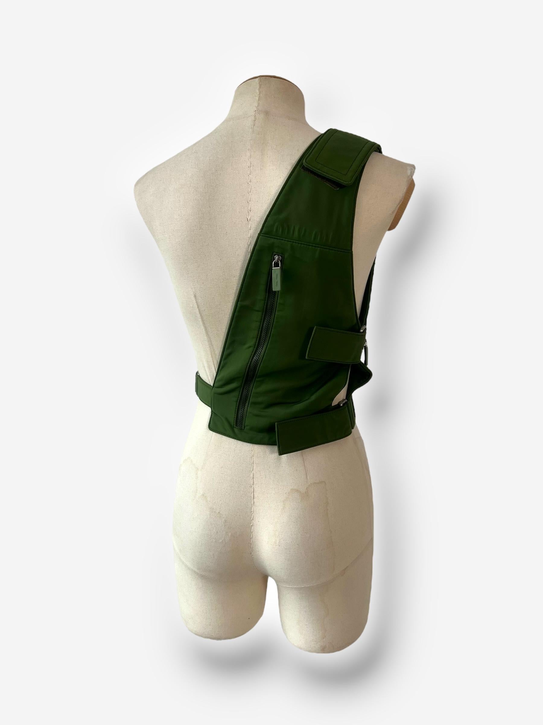 This rare Miu Miu chest rig bag from the SS99 collection offers both style and utility with its unique design. Crafted in a striking military green, the bag features a shoulder wrap style with multiple cargo pockets and zippered compartments on both