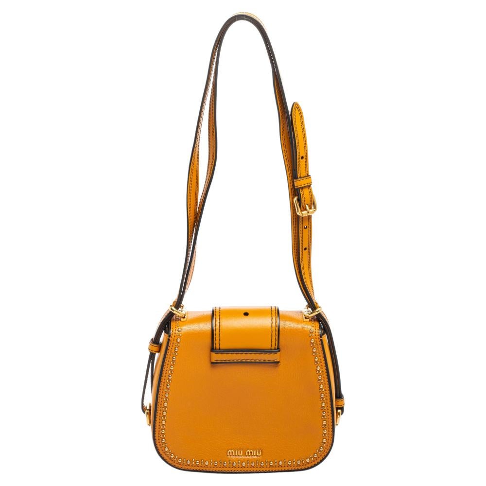 Gold-tone metal studs and an embellished buckle-like accent at the front highlight this Miu Miu Dahlia bag beautifully. It is made of leather and held by a crossbody strap.

Includes: Original Dustbag, Original Box

