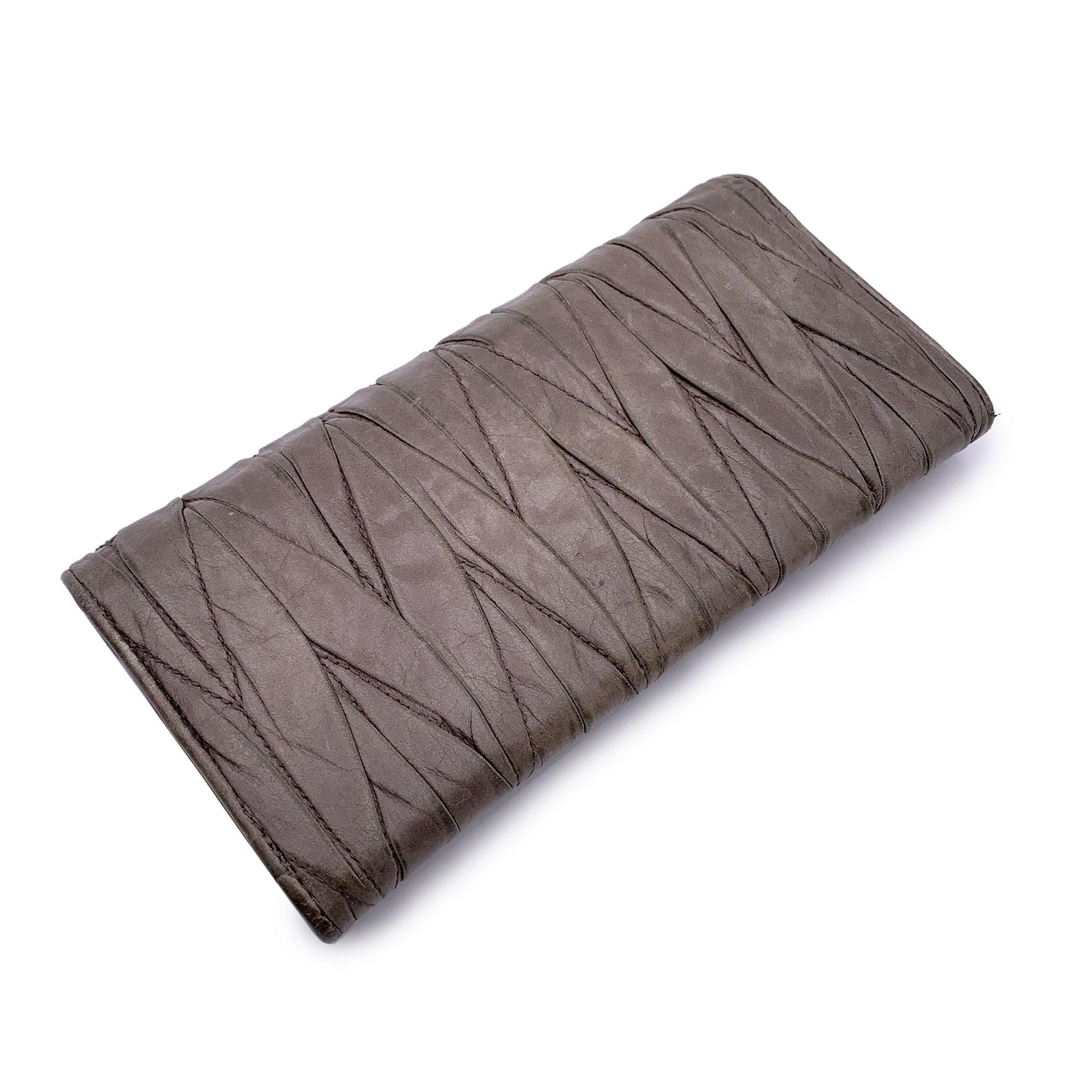 Taupe matelassé leather wallet MIU MIU. Light distressed effect on leather and classic continental shape. Gold metal MIU MIU lettering logo on the front Flap with button closure on the front . 12 credit card slots , 1 side open section under the