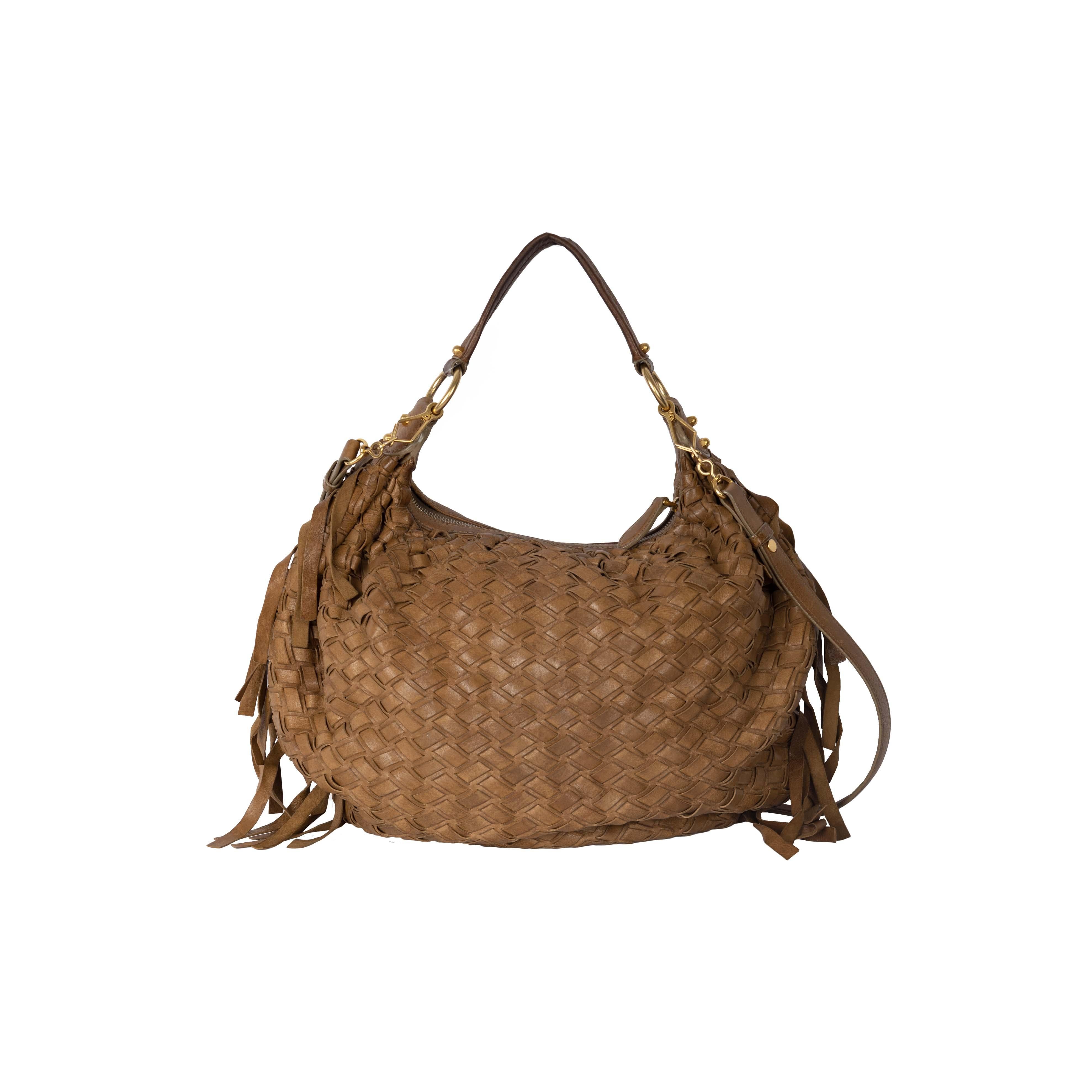 The Miu Miu Woven Leather Fringe Hobo features panels interwoven with a hobo bag structure. Adding the Miu Miu touch, the corners have frills attached. The bag can be handled as a purse with a short strap or can be worn crossbody with a long