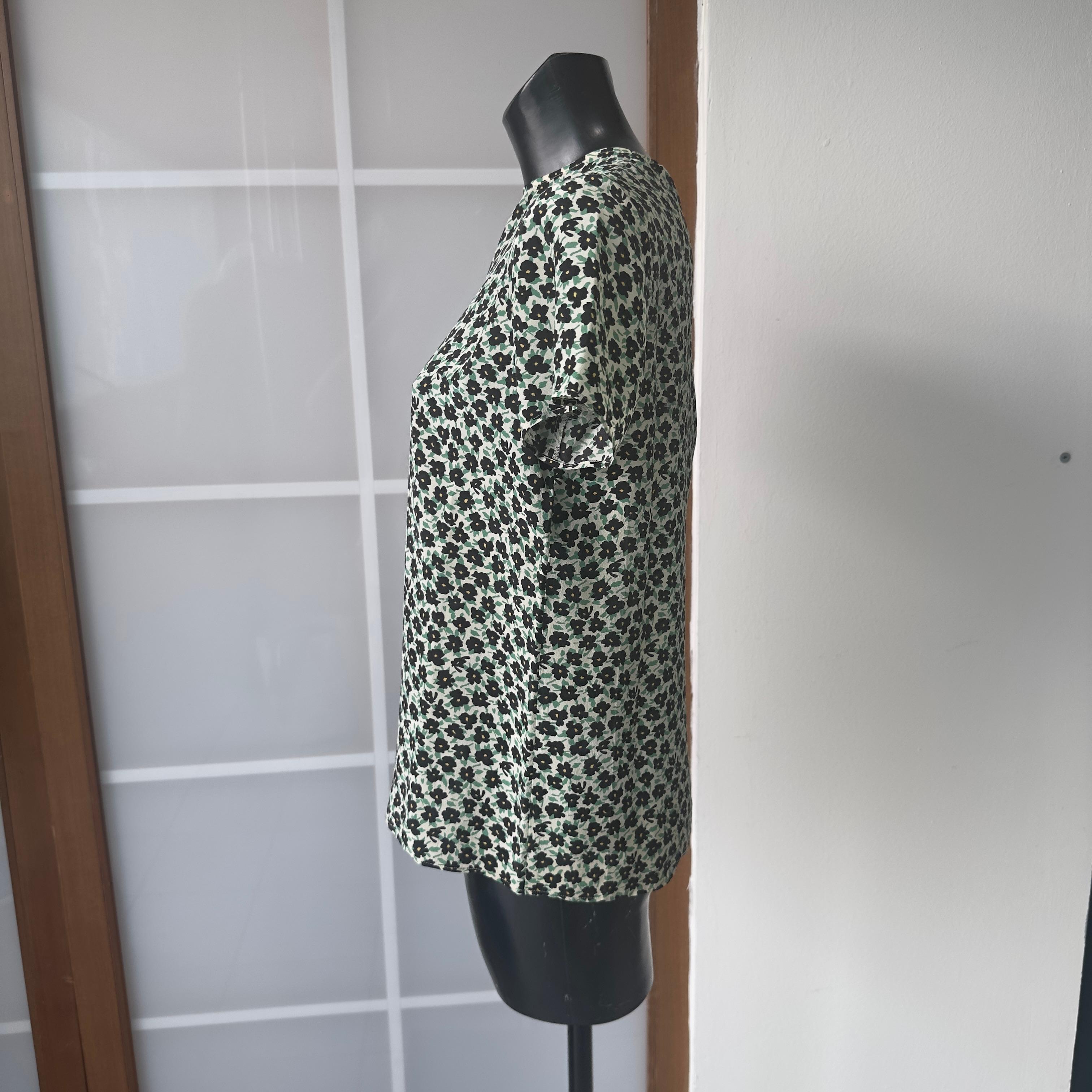 Un pezzo d’archivio rivisitato con charme contemporaneo.
Questa rara blusa in seta fa parte della capsule collection Miu Miu x Ken Scott, un omaggio all’iconico “giardiniere della moda” che ha ridefinito la stampa floreale negli anni ’60 e ’70. La