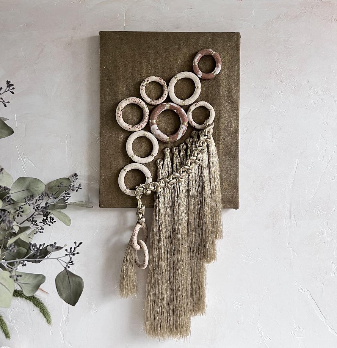A unique combination of materials adorning a hand painted linen canvas would make a great addition to a wall gallery or hung by itself in small wall space. 

The hand built stoneware rings are embroidered to the surface, with added details of