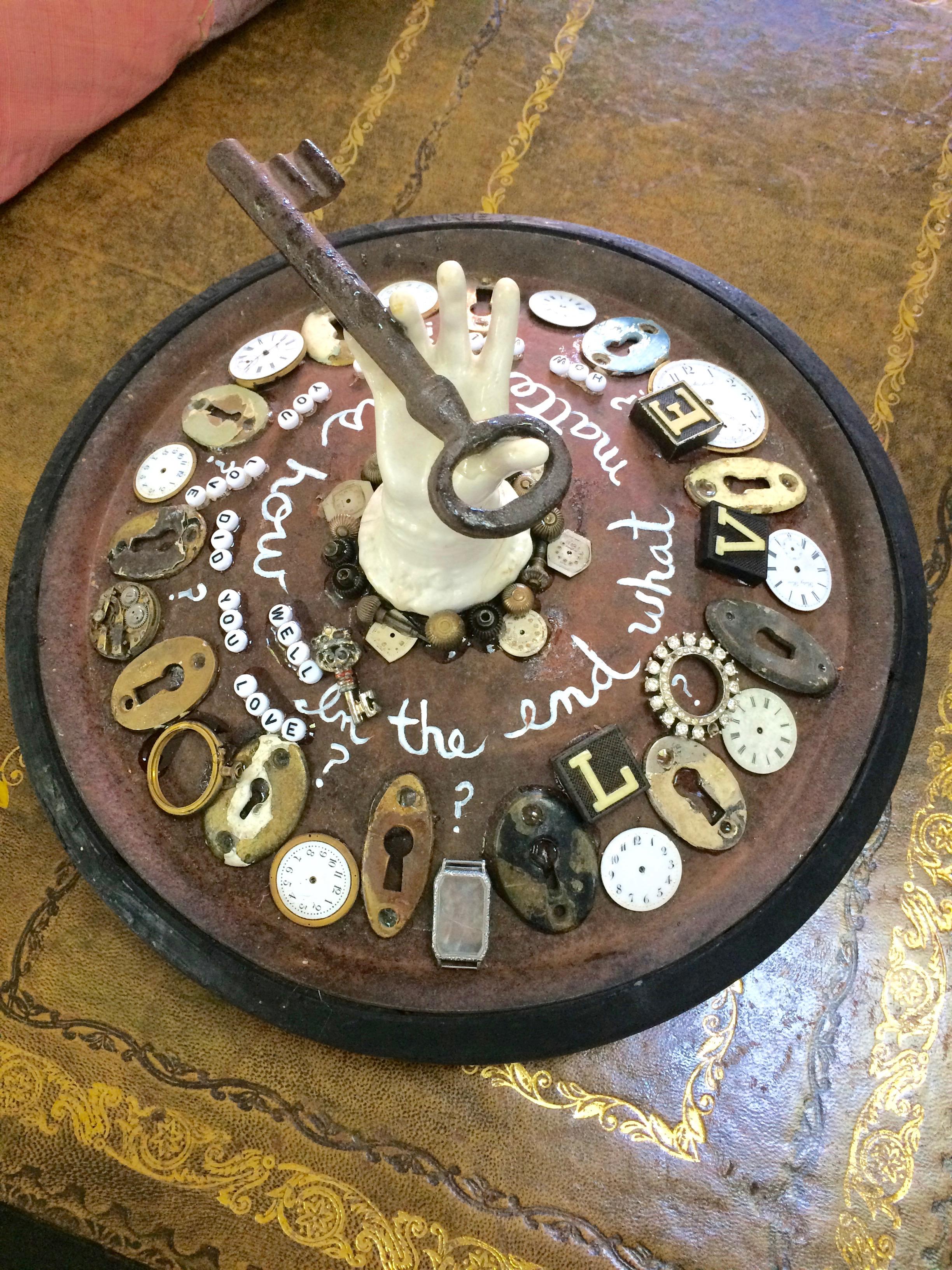 Sculpture d'objets trouvés merveilleusement imaginative ayant pour base une vieille roue de boîte à savon, incrustée de trous de serrure, de cadrans d'horloge, d'une main en porcelaine antique sortant du centre avec une énorme clé, et d'un message