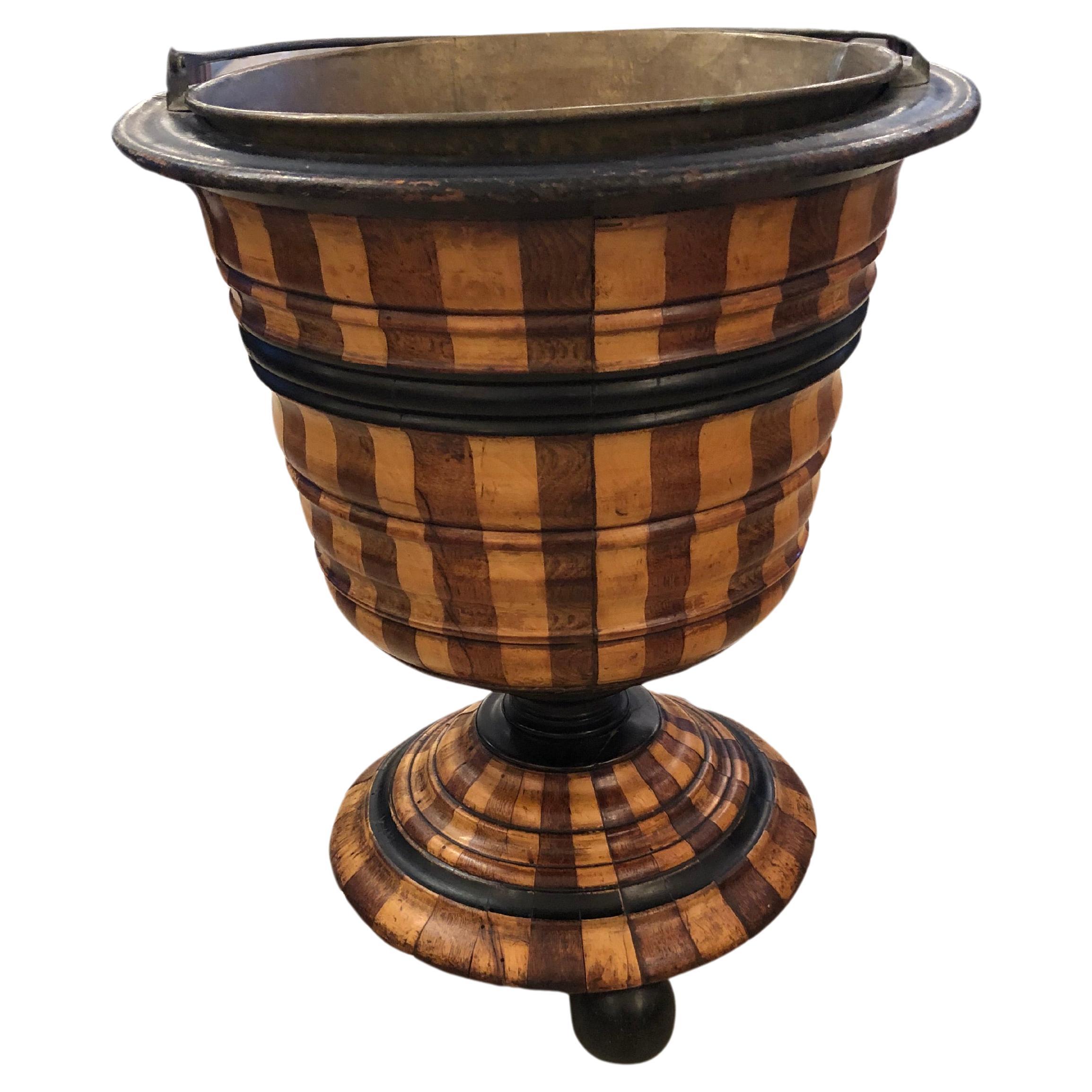 Handsome mixed wood urn shaped planter having dark and light striped pattern and ball feet.  There's a copper pail liner.  A metal handle makes the whole planter 23
