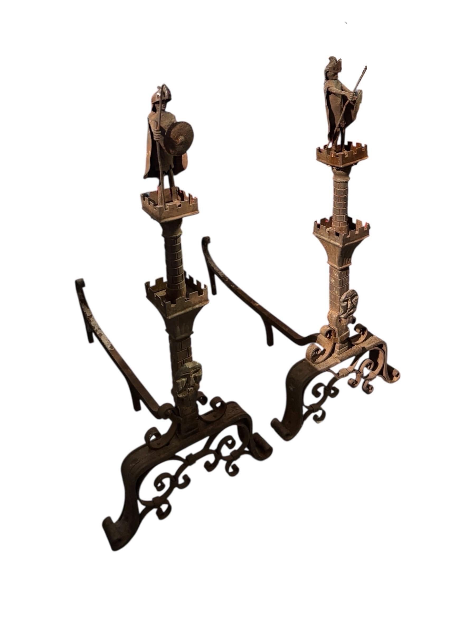 A pair of wrought iron andirons circa 1890, removed from a Mizner estate in Palm Beach, FL. Medieval knights with swords raised in a gesture of victory top castle turrets, above scrolled wrought iron bases.