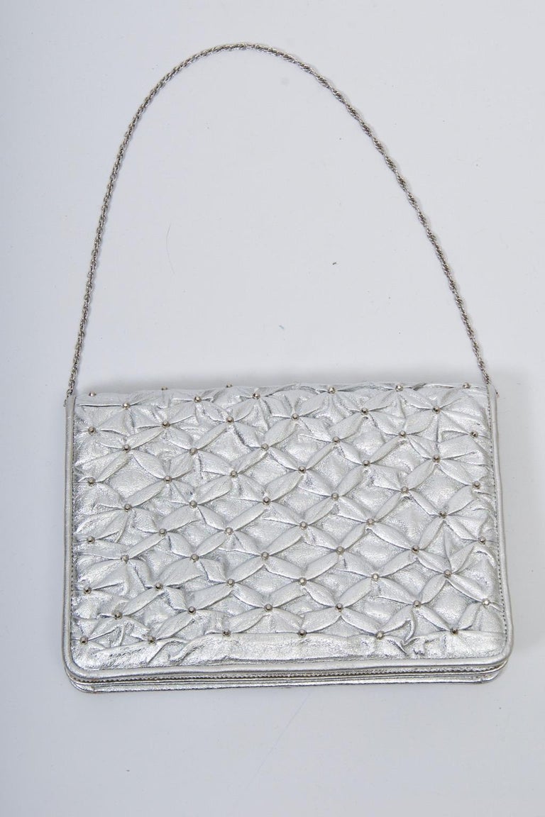 Morris Moskowitz clutch in silver leather that has been quilted in a star design. The foldover clutch has a divided interior, one side with zippered compartment. A thin silver chain converts the clutch to a handled version.