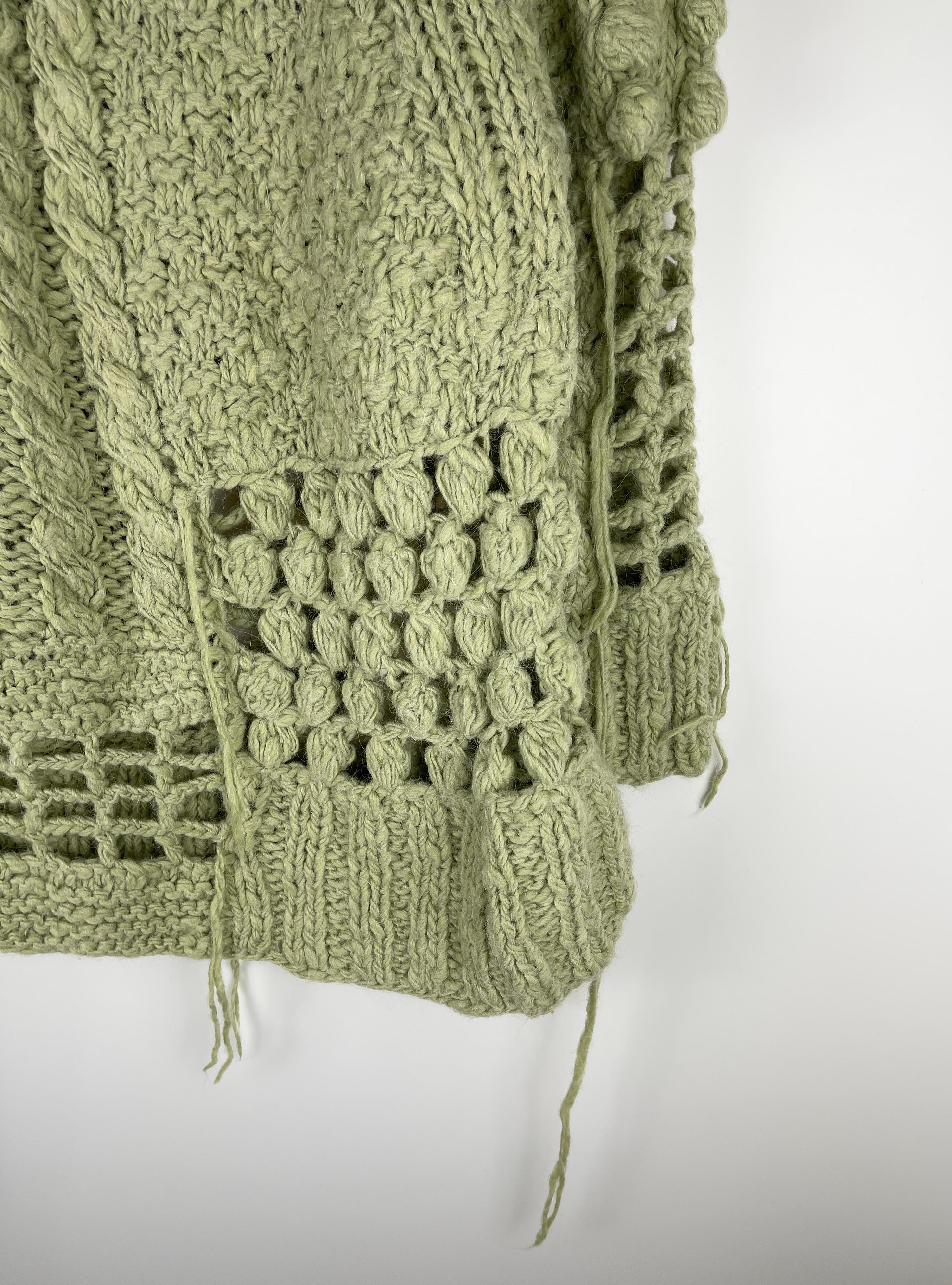 Long sleeve rib knit, cable knit, waffle knit, and open knit alpaca and wool-blend sweater in pale green. Distressing and extended thread and knit ball detailing throughout. Rib knit crewneck collar and cuffs. The item is made for a unisex